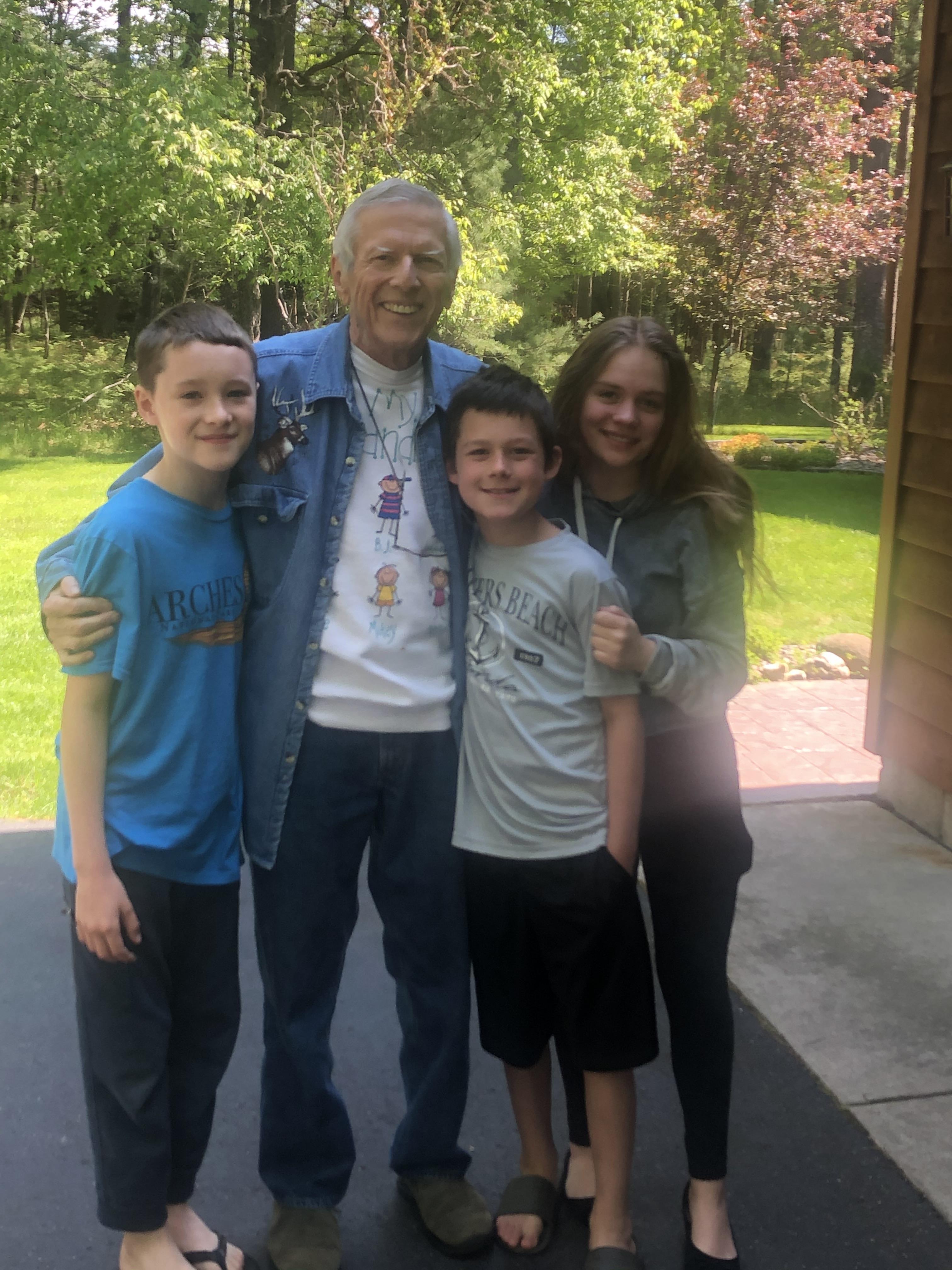 Three grandchildren pose happily with their grandfather in a vibrant outdoor setting.