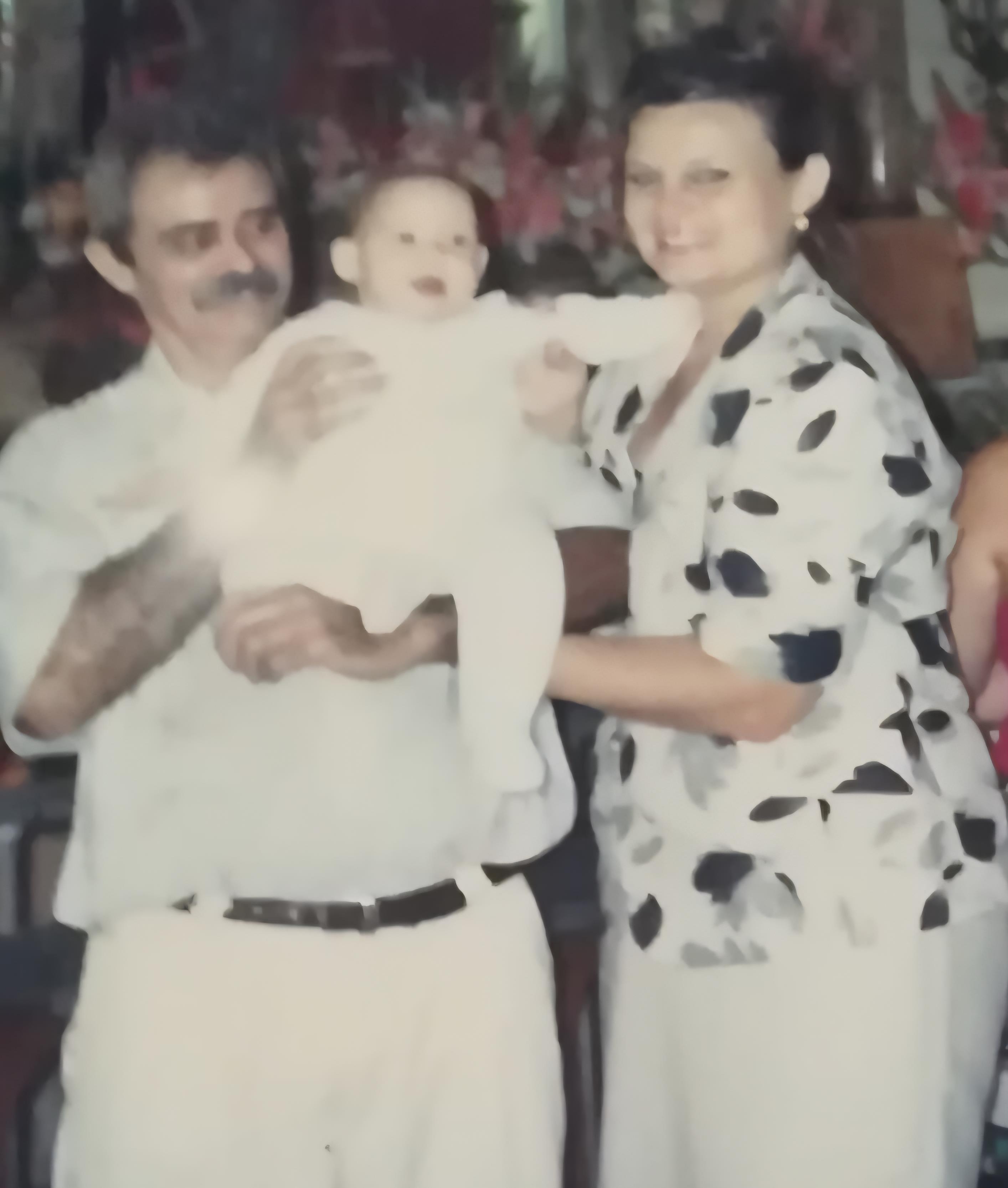 A loving couple holds a baby while celebrating with friends in a vibrant atmosphere.