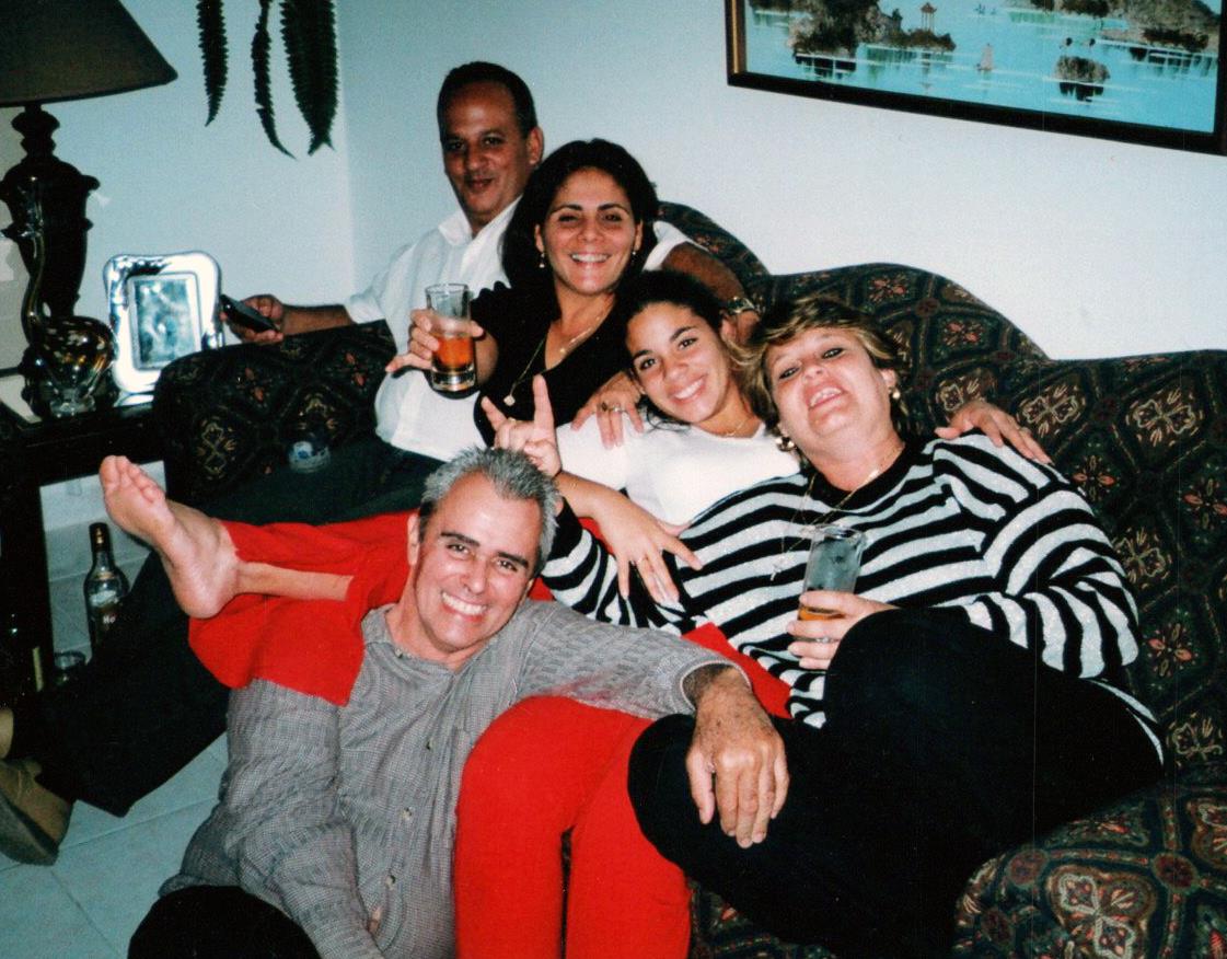 Five friends are sitting comfortably on a couch, sharing laughs and beverages while relaxing.