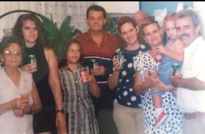 A diverse group of family members celebrate together, holding drinks and smiling warmly.