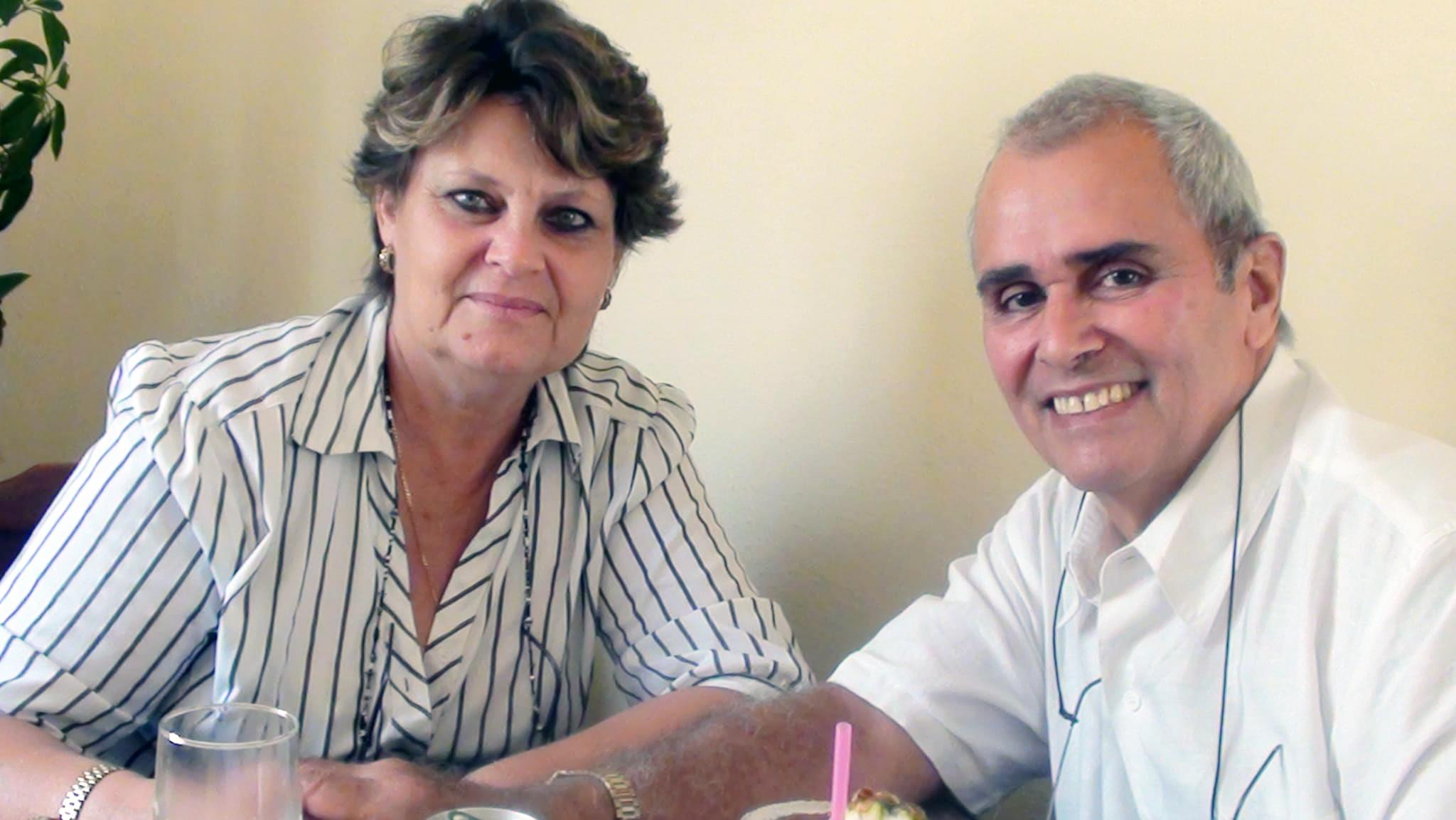 A cheerful couple smiles while seated at a table, enjoying each other's company during lunch.