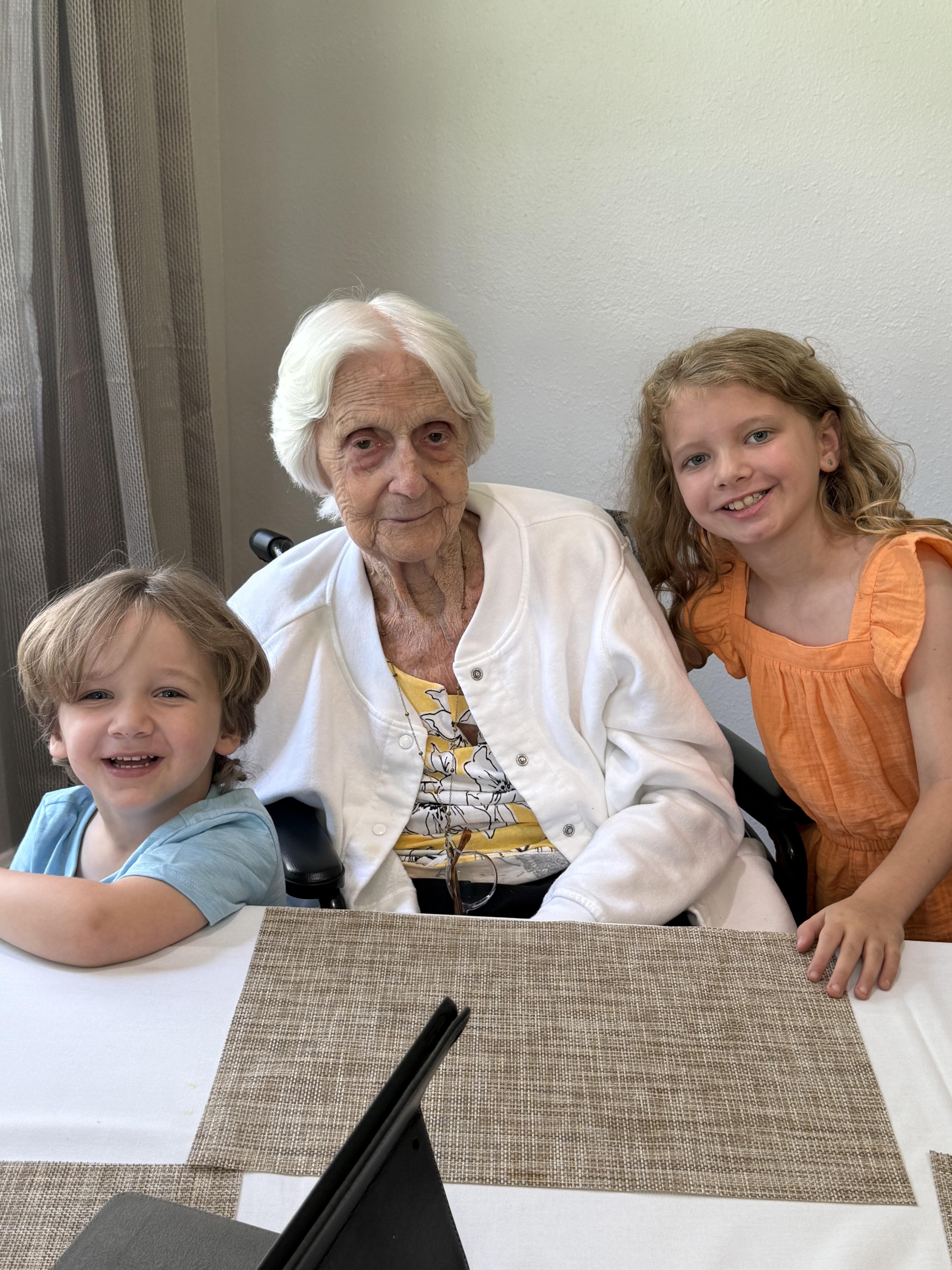 Two cheerful children sit with an elderly woman in a cozy room, sharing a joyful moment together.