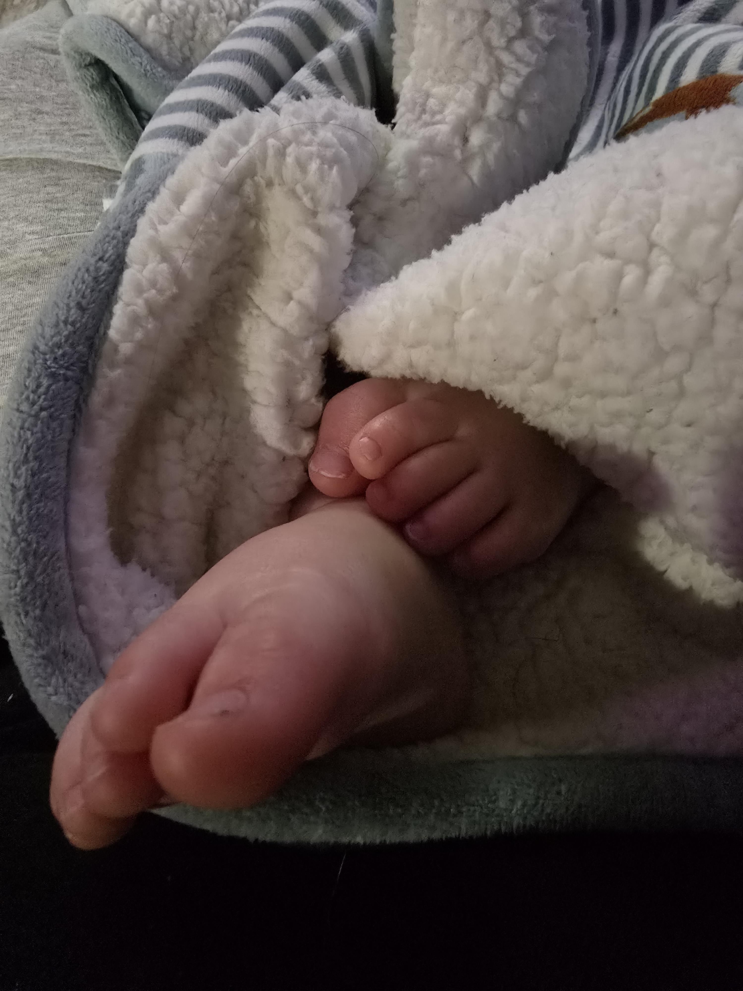 Cozy baby feet are tucked inside a soft blanket, creating a warm and serene atmosphere at home.