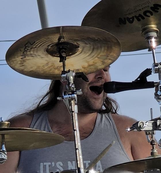 Drummer sings and plays energetically on stage during a vibrant outdoor concert.
