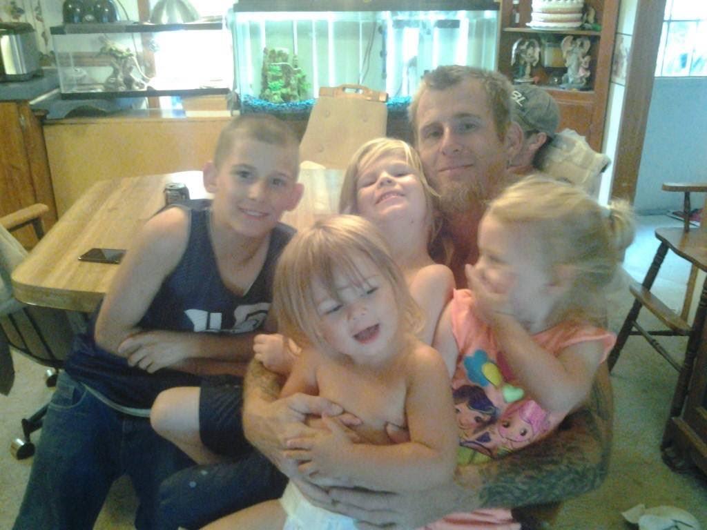 A man embraces four cheerful children in a warm, inviting home setting filled with joy.