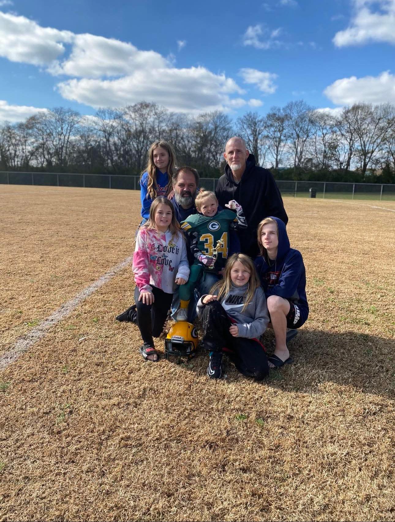A cheerful gathering of family and friends posing together on a football field under blue skies.