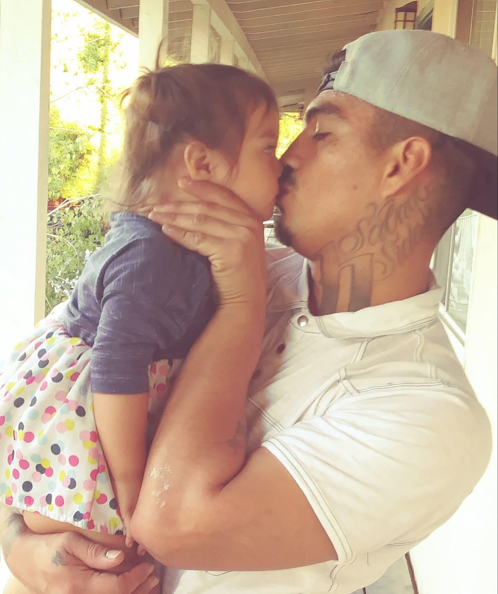 A father embraces his young daughter, sharing a sweet kiss while enjoying their outdoor space.