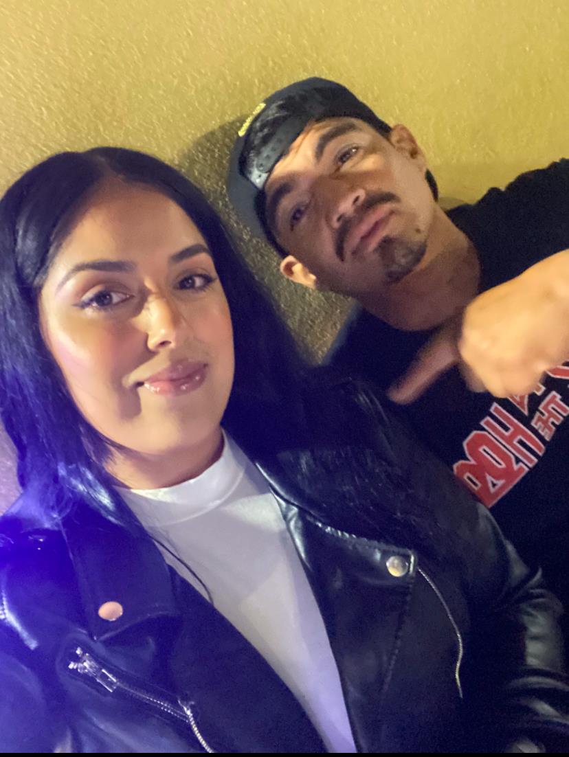 A couple smiles while posing for a casual selfie at night, showcasing their stylish outfits.