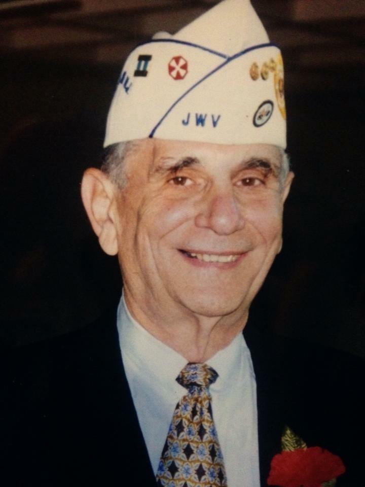 Elderly veteran in a ceremonial cap smiles warmly during an event honoring service members.