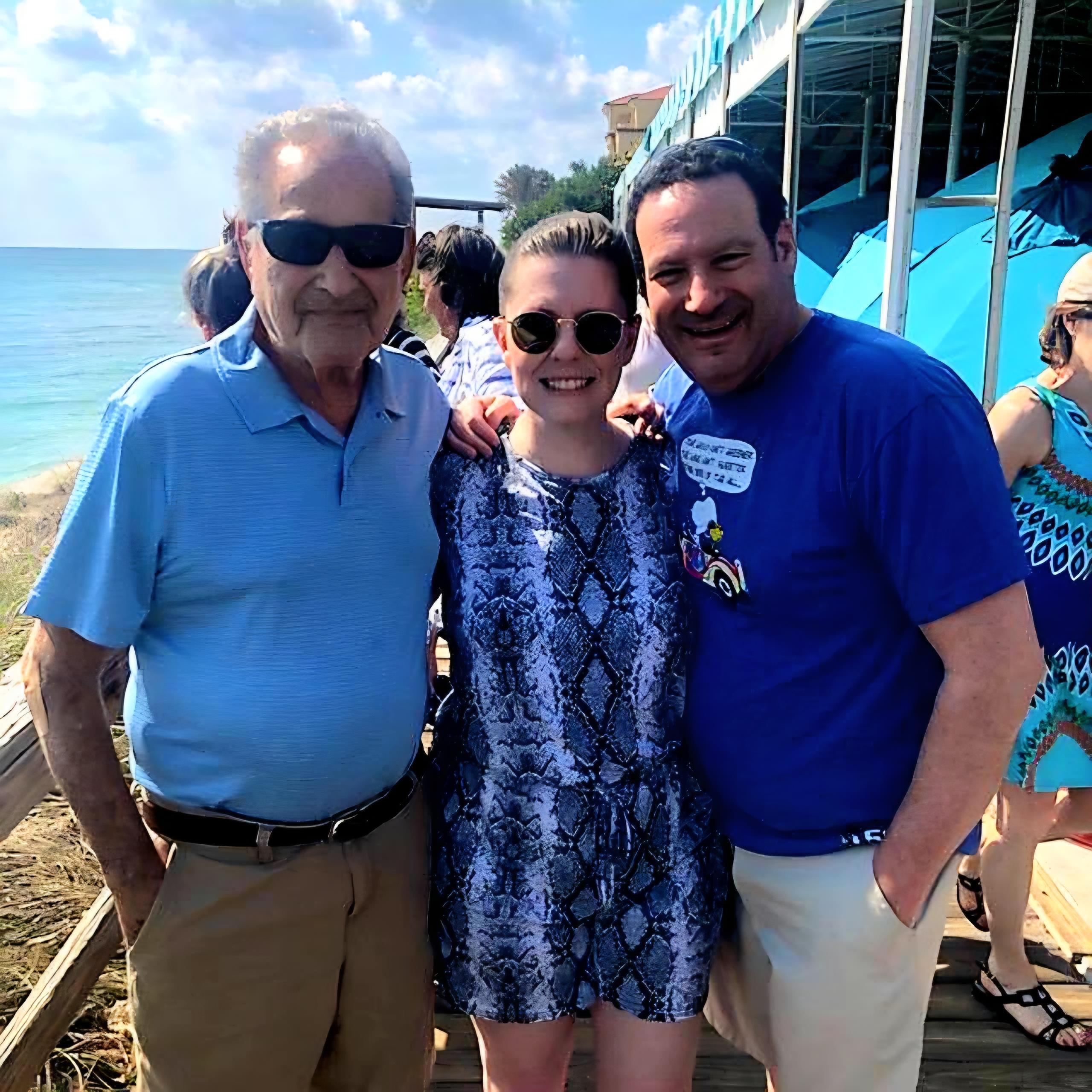 Three friends pose for a cheerful photo on a sunny beach boardwalk during a fun outing.