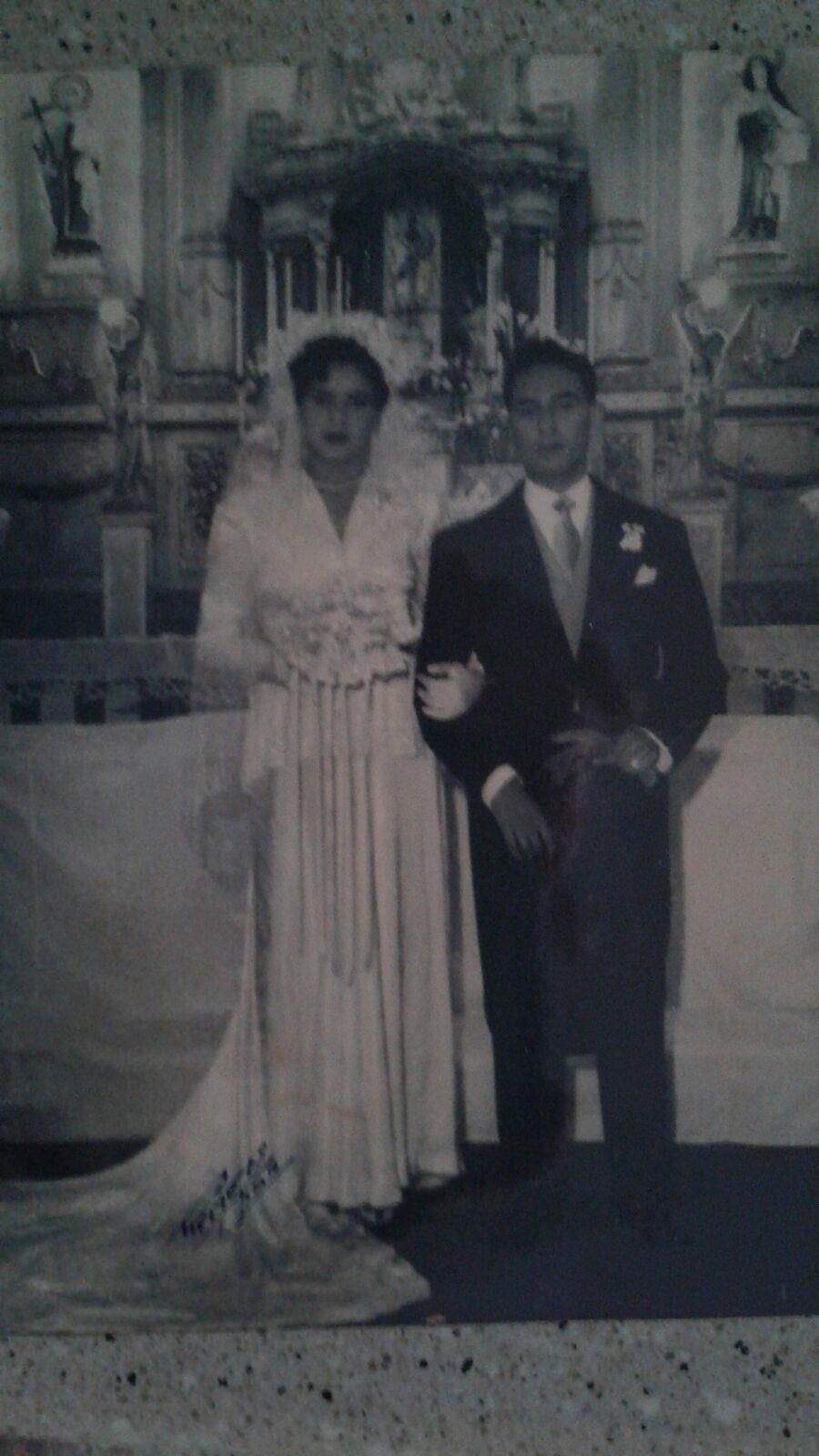 A couple in elegant wedding attire poses inside a beautifully decorated church altar.