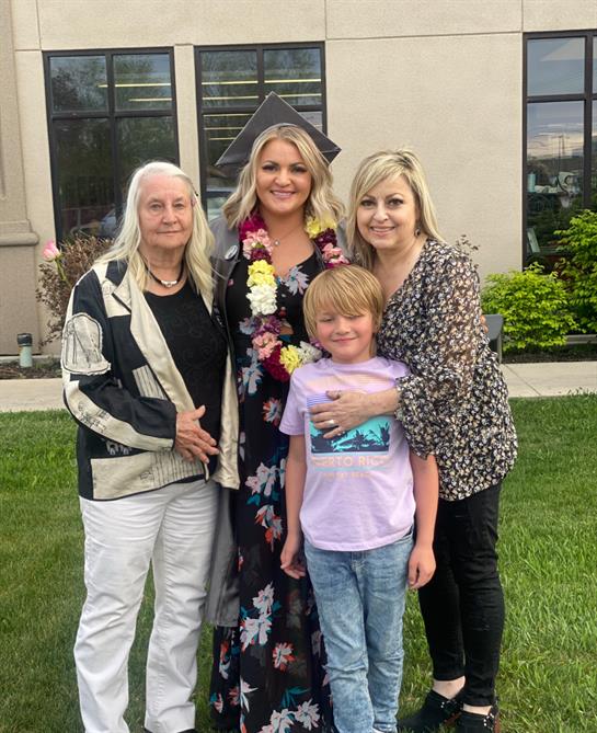 A woman in a graduation cap and gown with a boy and two women in front of a building
