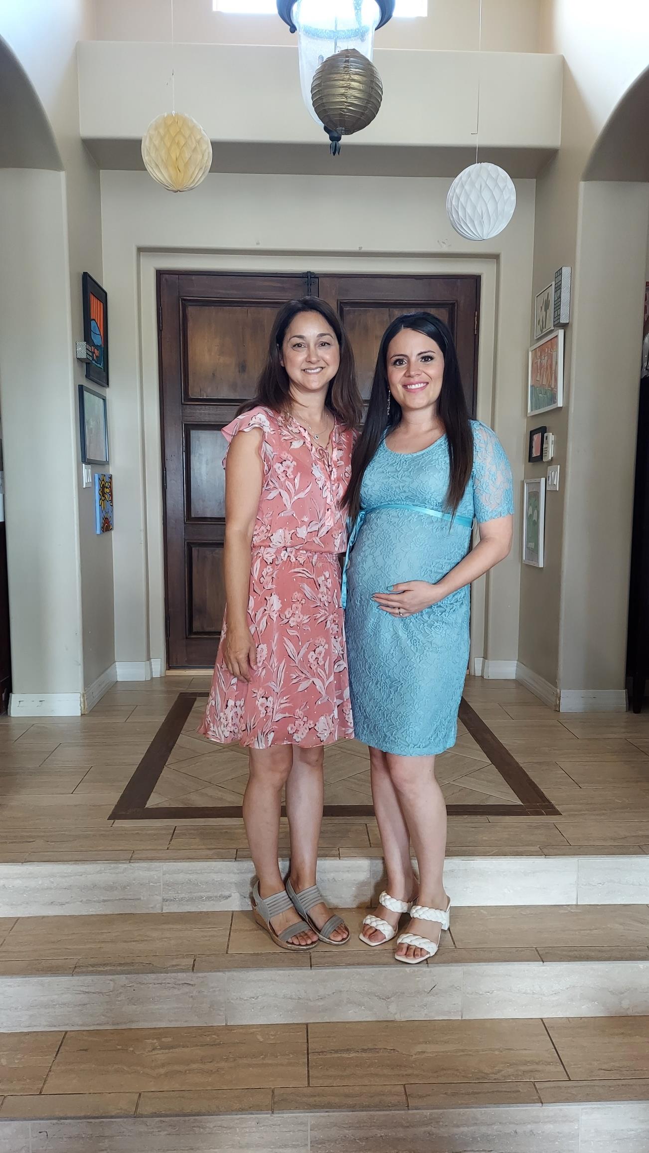 Two friends stand together in a cozy home entrance, one is pregnant and glowing with joy.