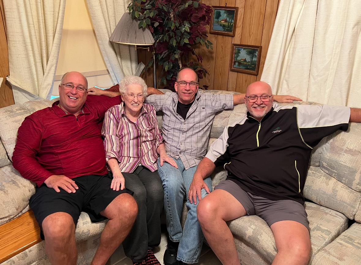 Four family members smile together on the sofa, celebrating their bond in a cozy room.