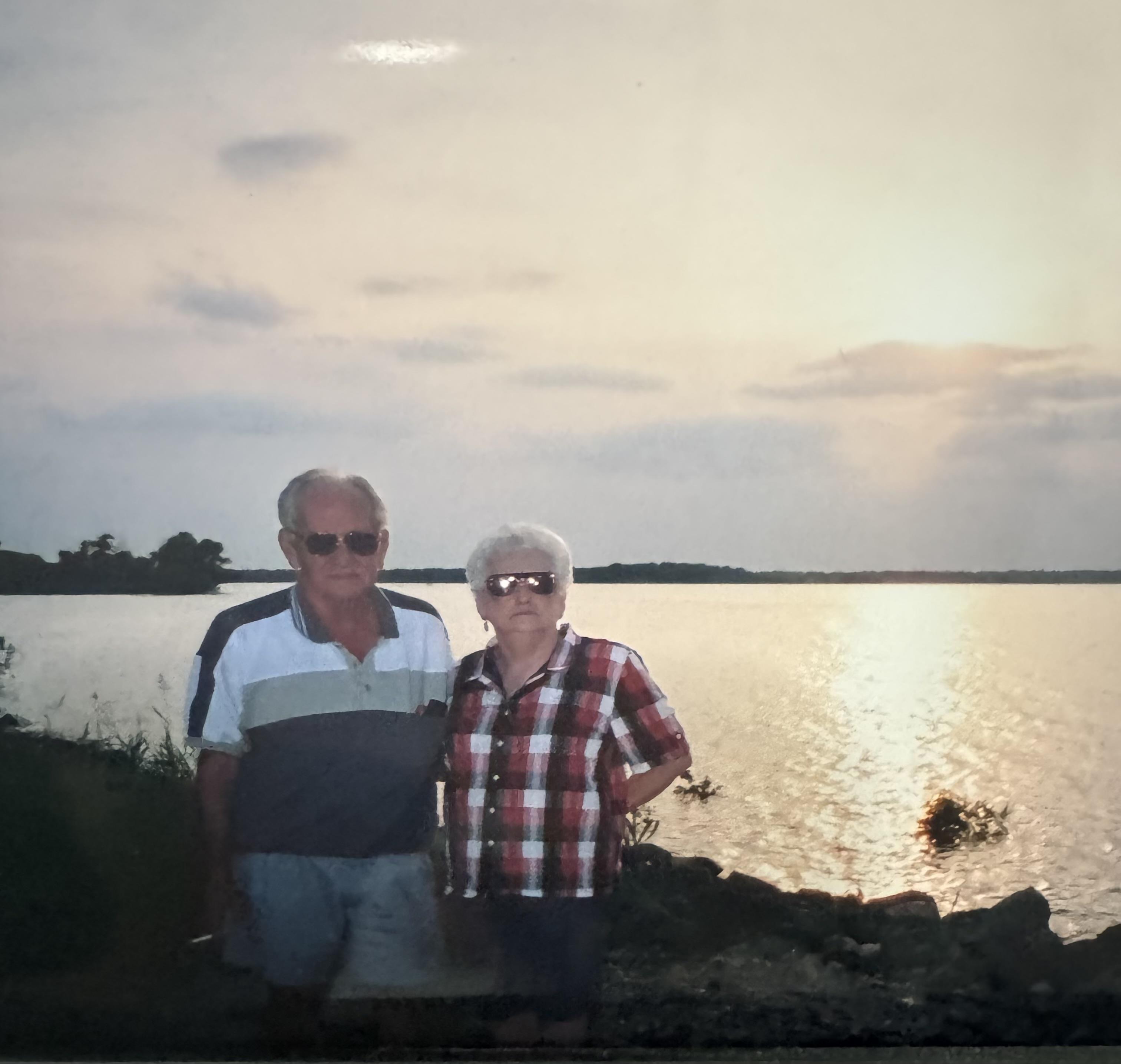 Senior couple stands by the lake, admiring the beautiful sunset glow.