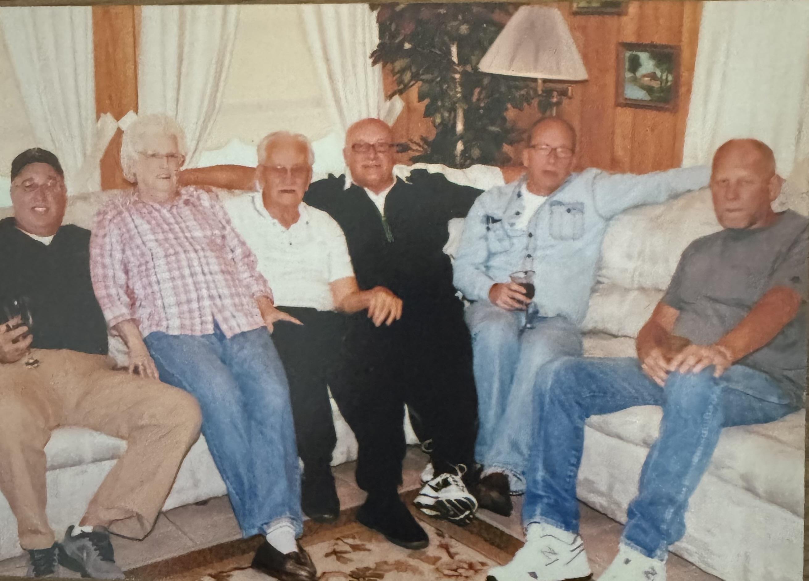 Friends relax on a sofa, sharing laughter and drinks in a warm home atmosphere.