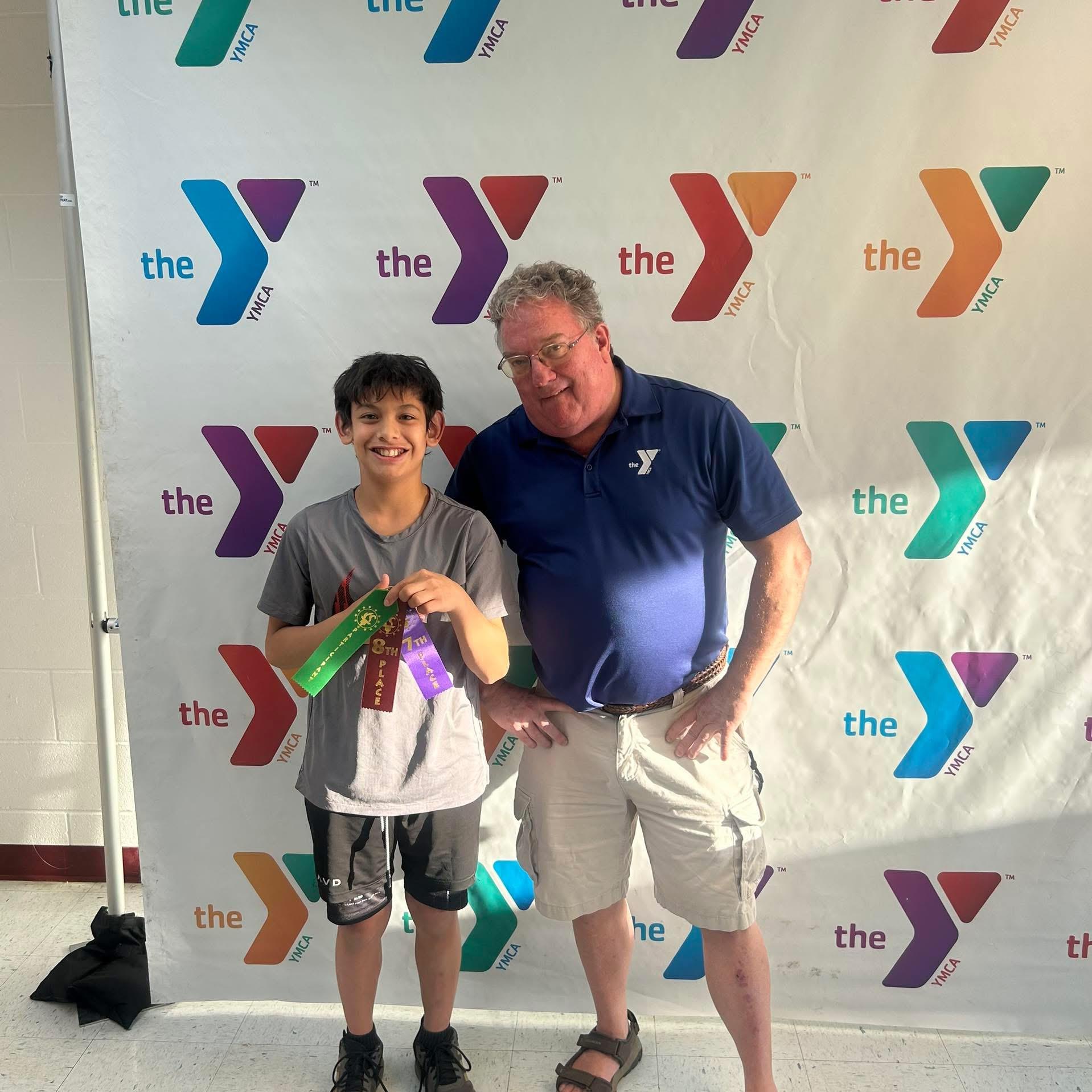 A young boy holds awards while standing next to his coach after a successful competition.