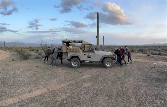 A group of people pushing a jeep in a desert