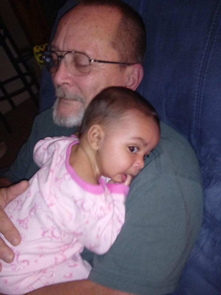 A grandfather gently holds his grandchild, both resting comfortably on a blue couch.