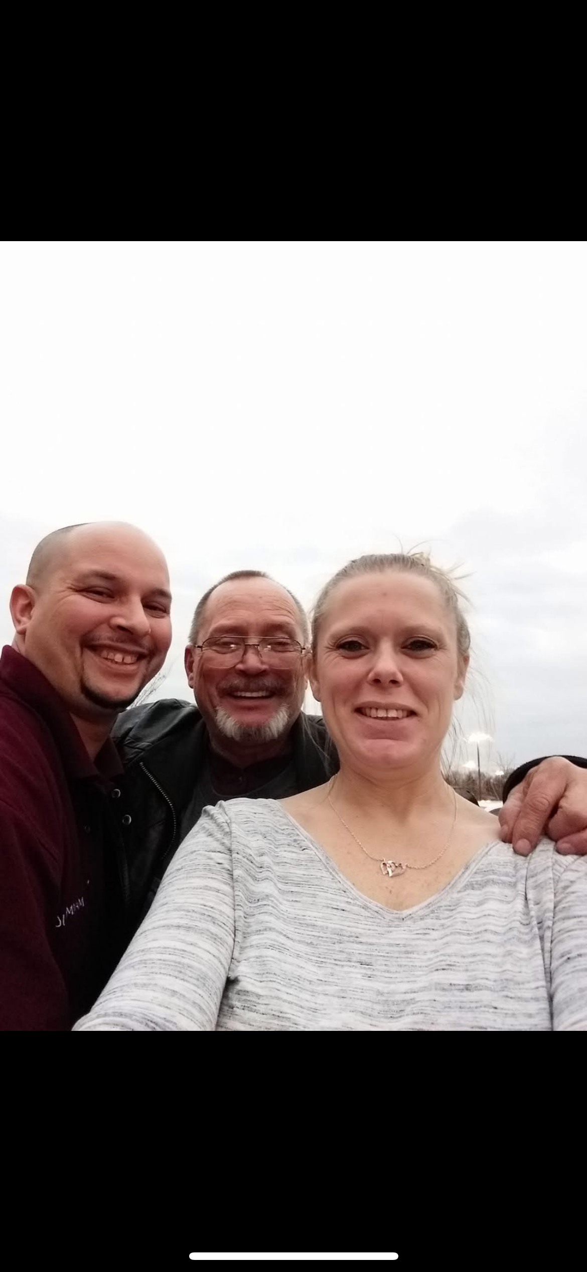 Three friends gather outdoors on a cloudy day, smiling and enjoying each other's company.