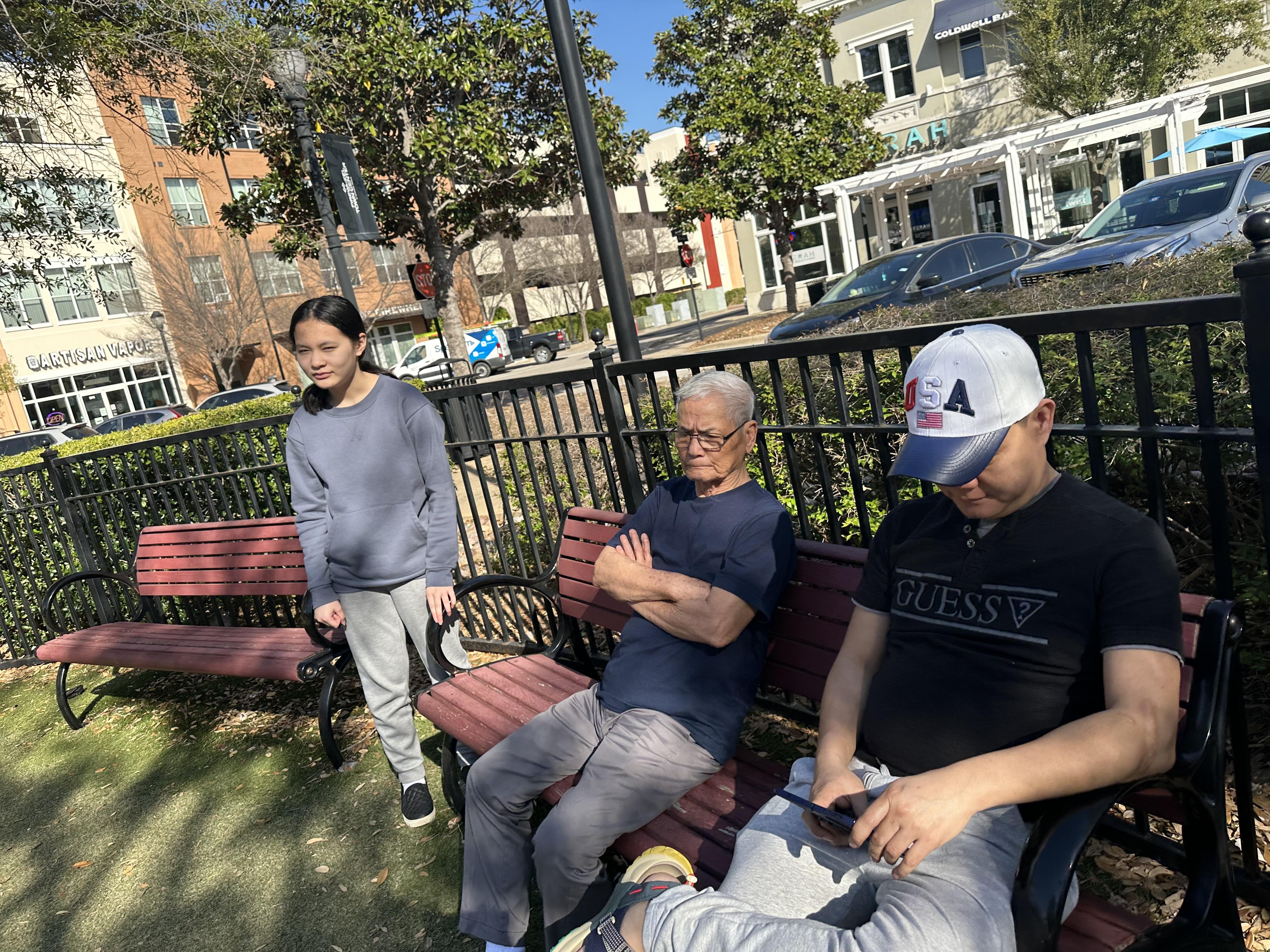 People relax on benches in a lively urban park under clear blue skies, enjoying their day.