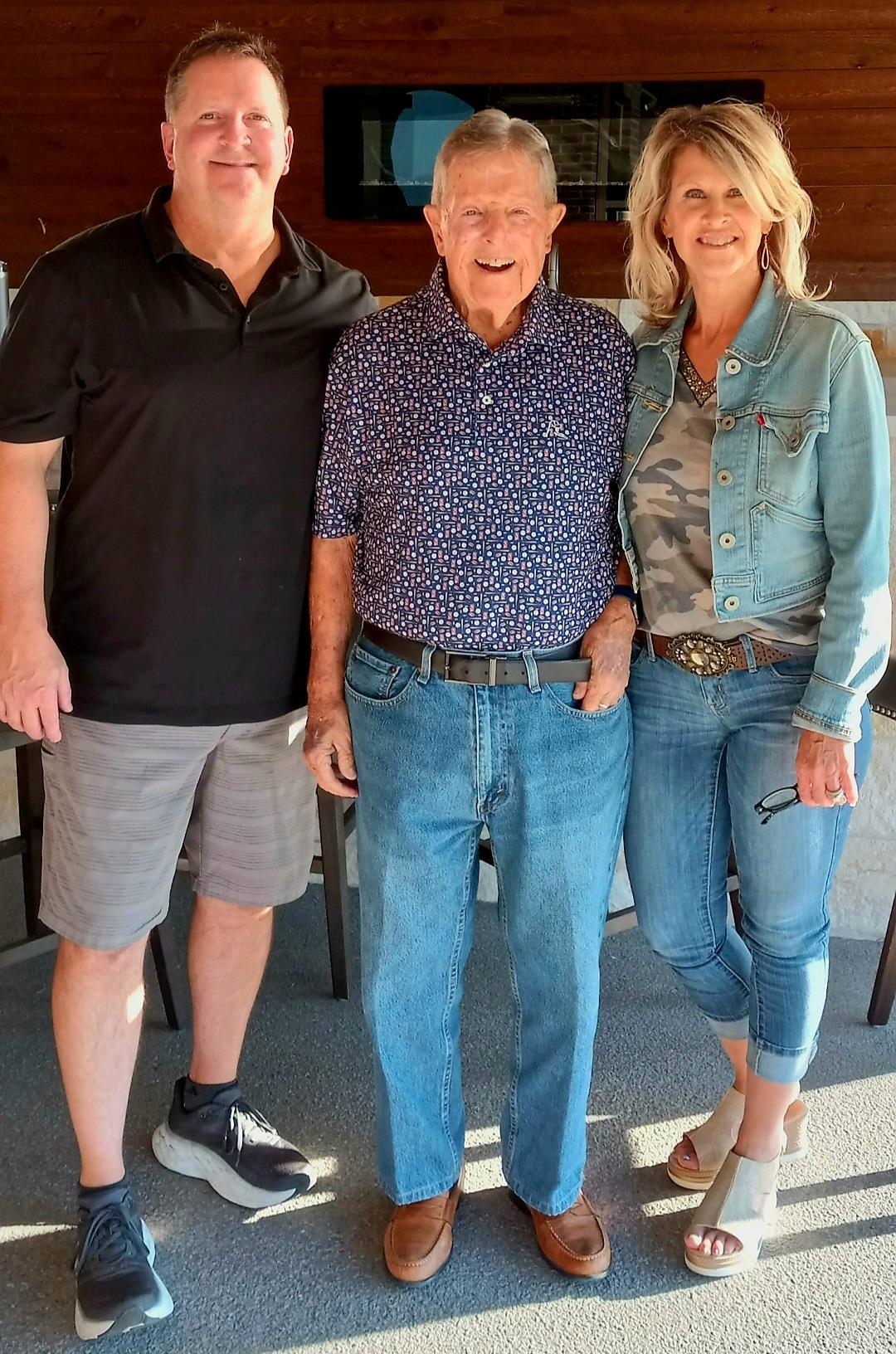 Three family members pose happily at a cozy outdoor venue, celebrating their bond and togetherness.