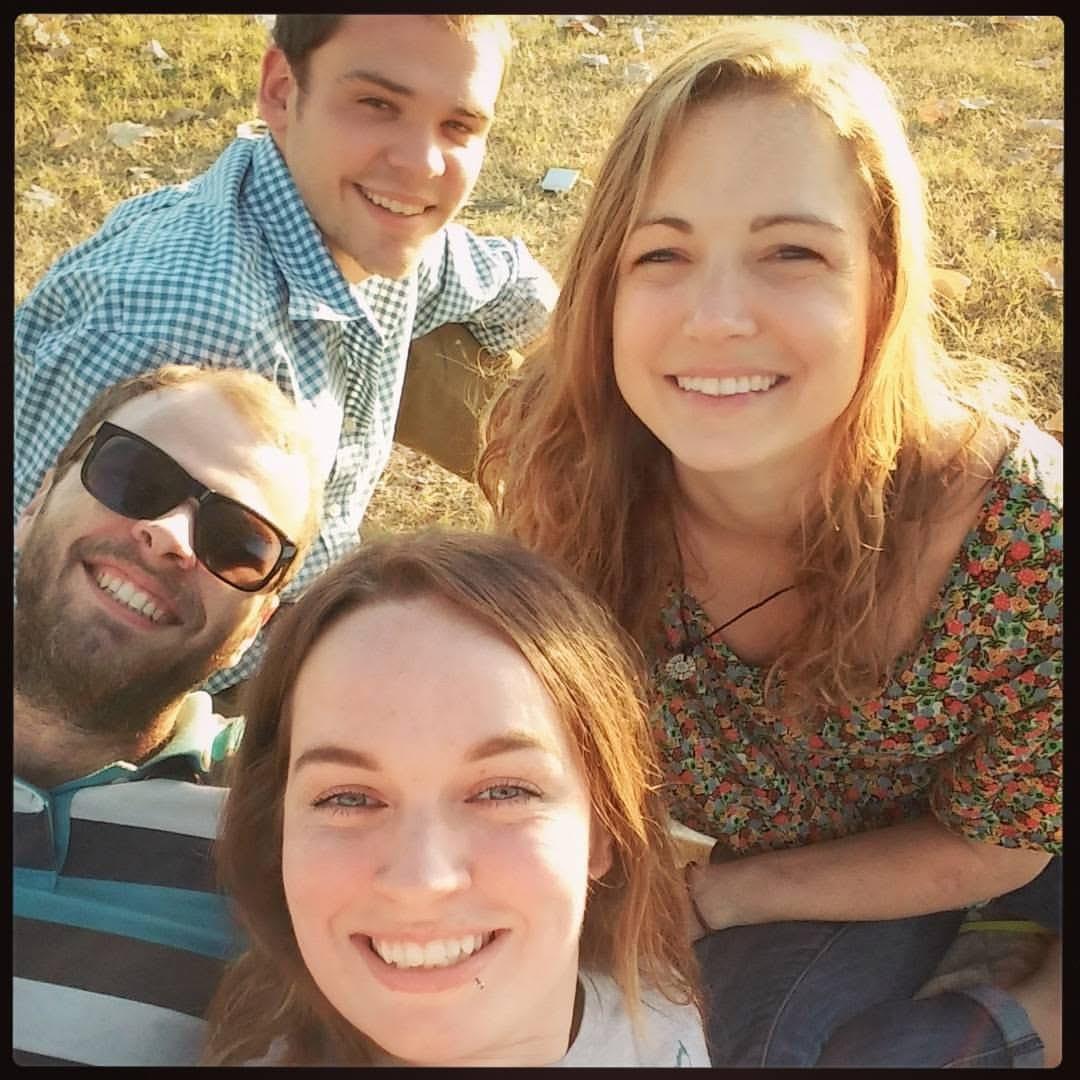Four friends smile happily while sitting together on the grass during a sunny day.