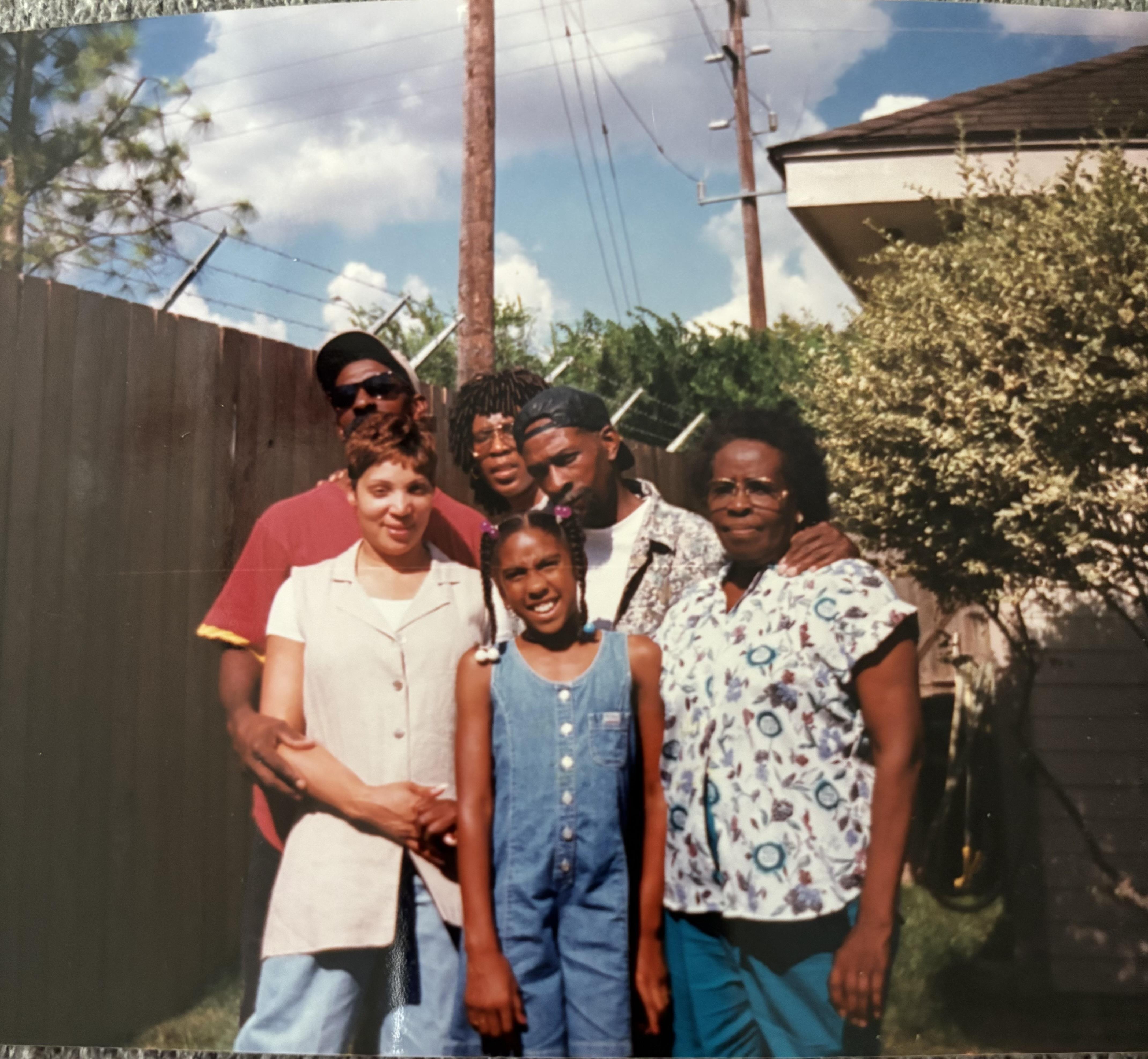 Five family members gather in a backyard, enjoying a sunny afternoon and smiling happily.