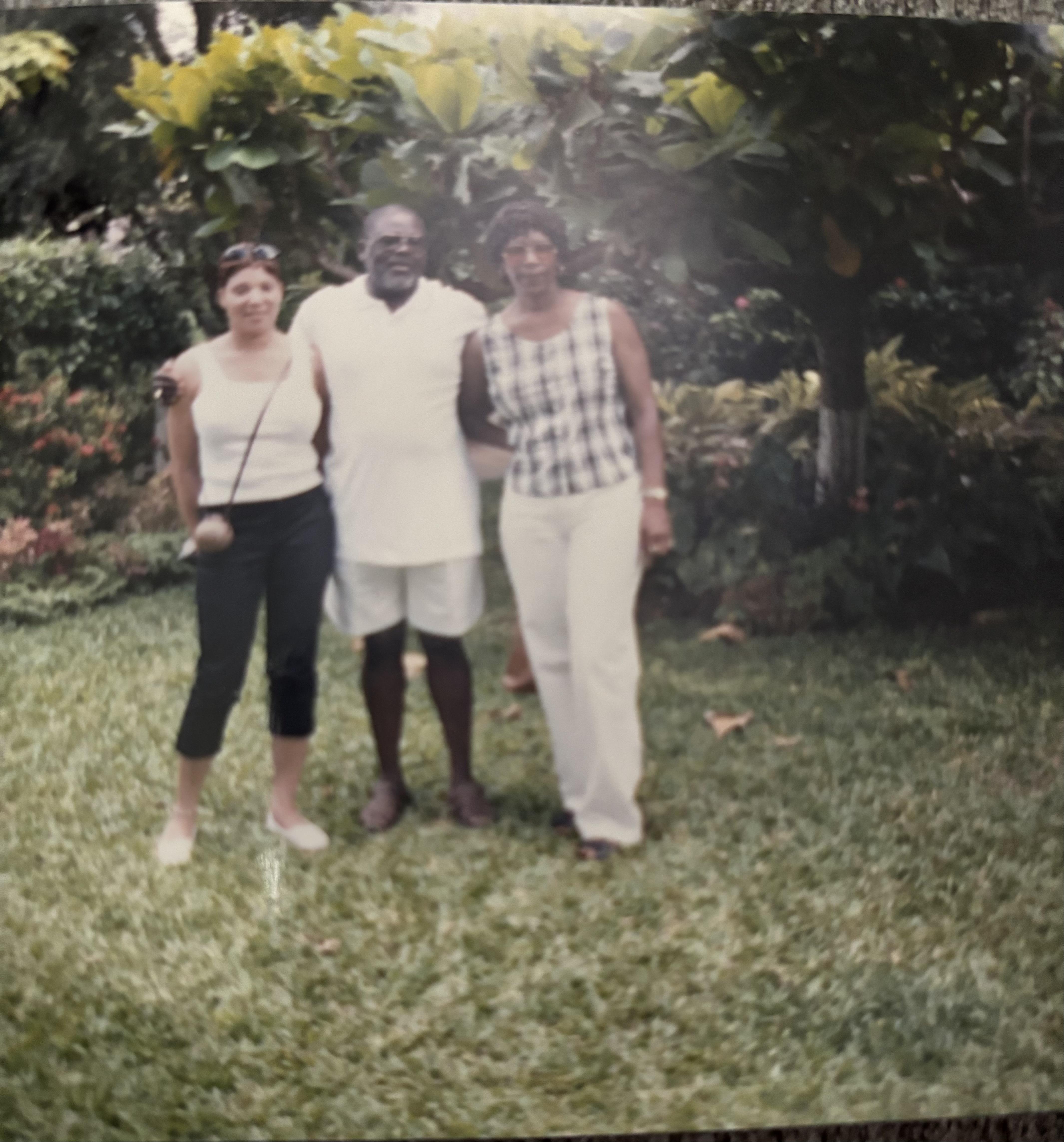 Three people pose together in a vibrant garden filled with greenery on a warm day.