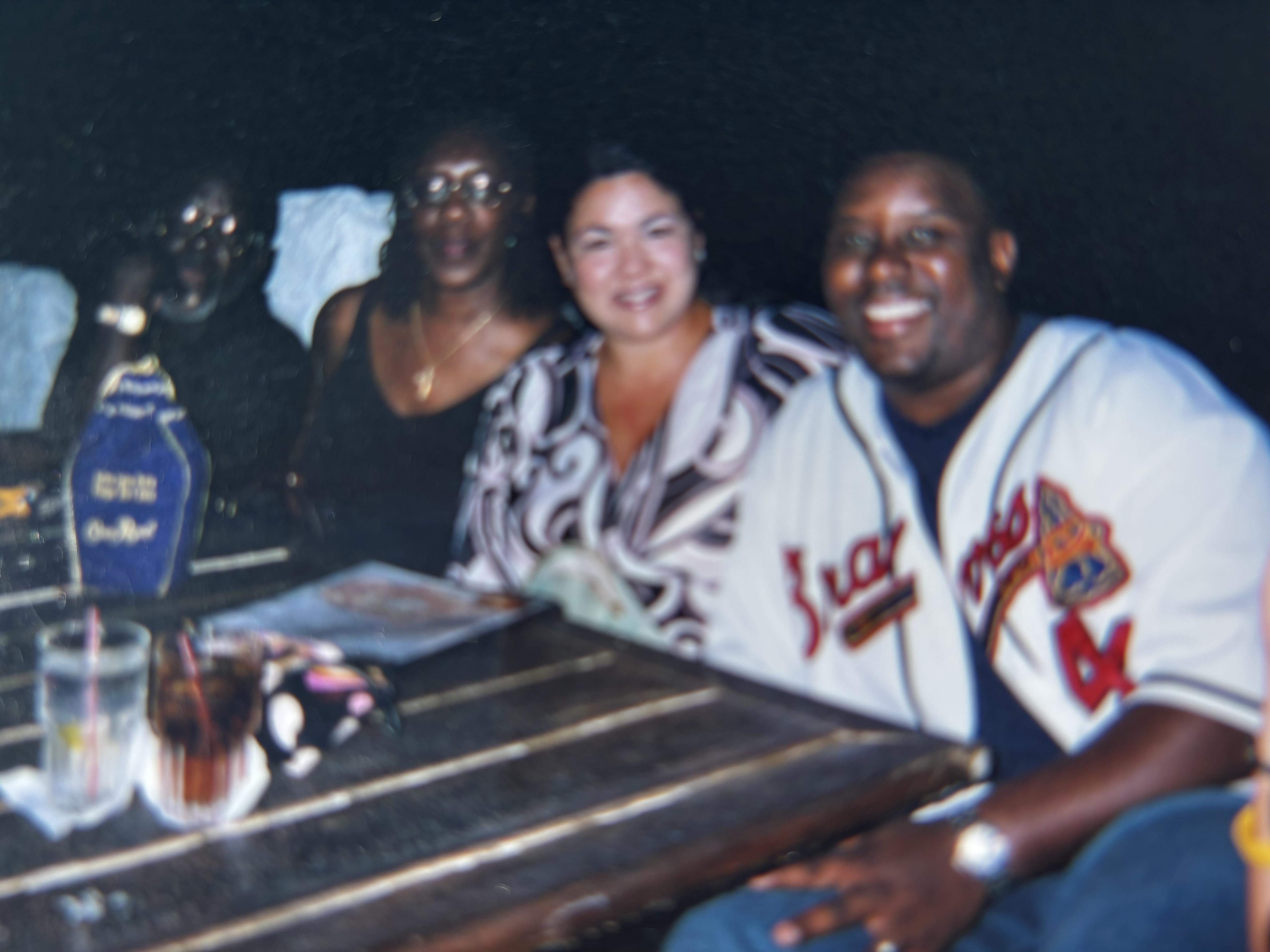 Four people share laughter and conversation at a coastal restaurant while enjoying drinks.