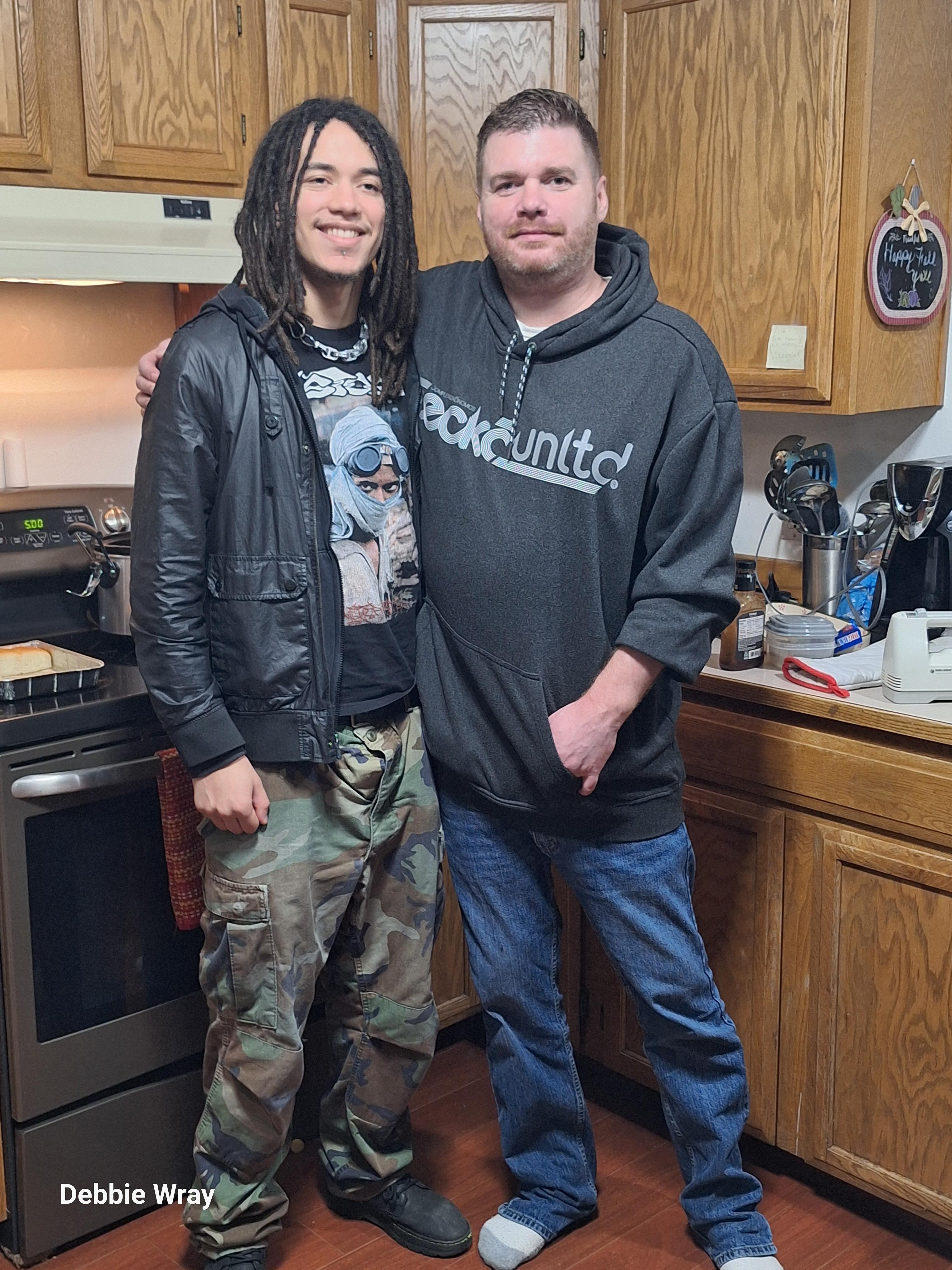 Two friends stand side by side in a warmly lit kitchen, enjoying a relaxed moment together.