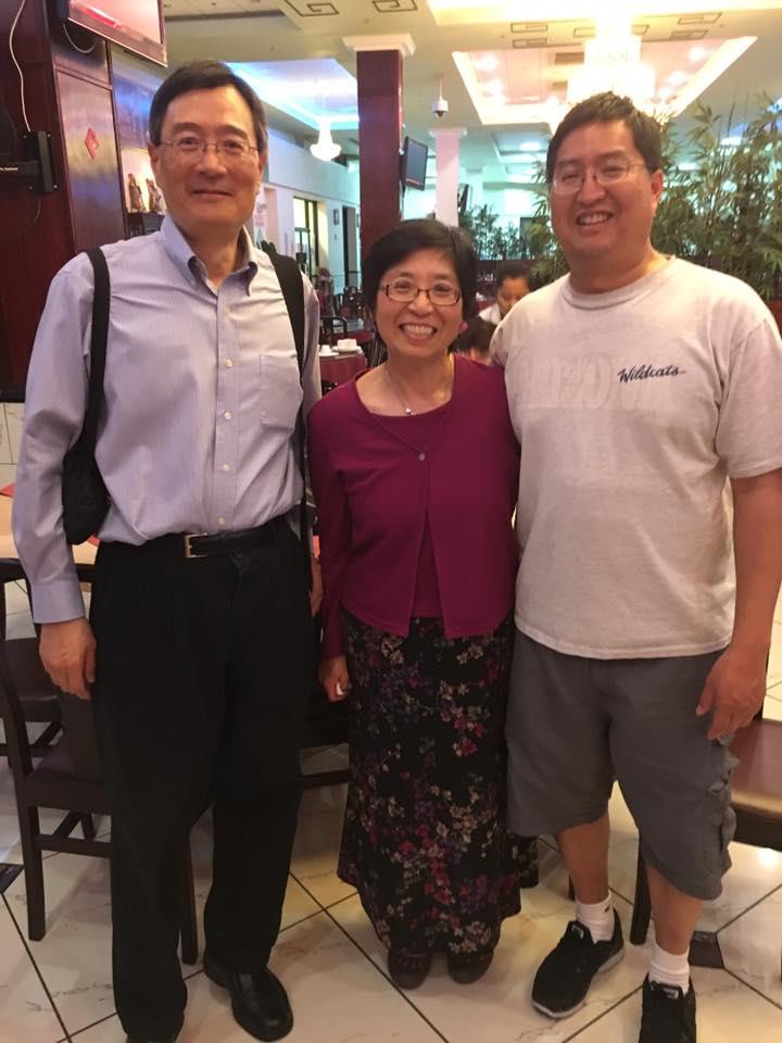 Three friends smile and pose together in a restaurant, enjoying a joyful reunion.