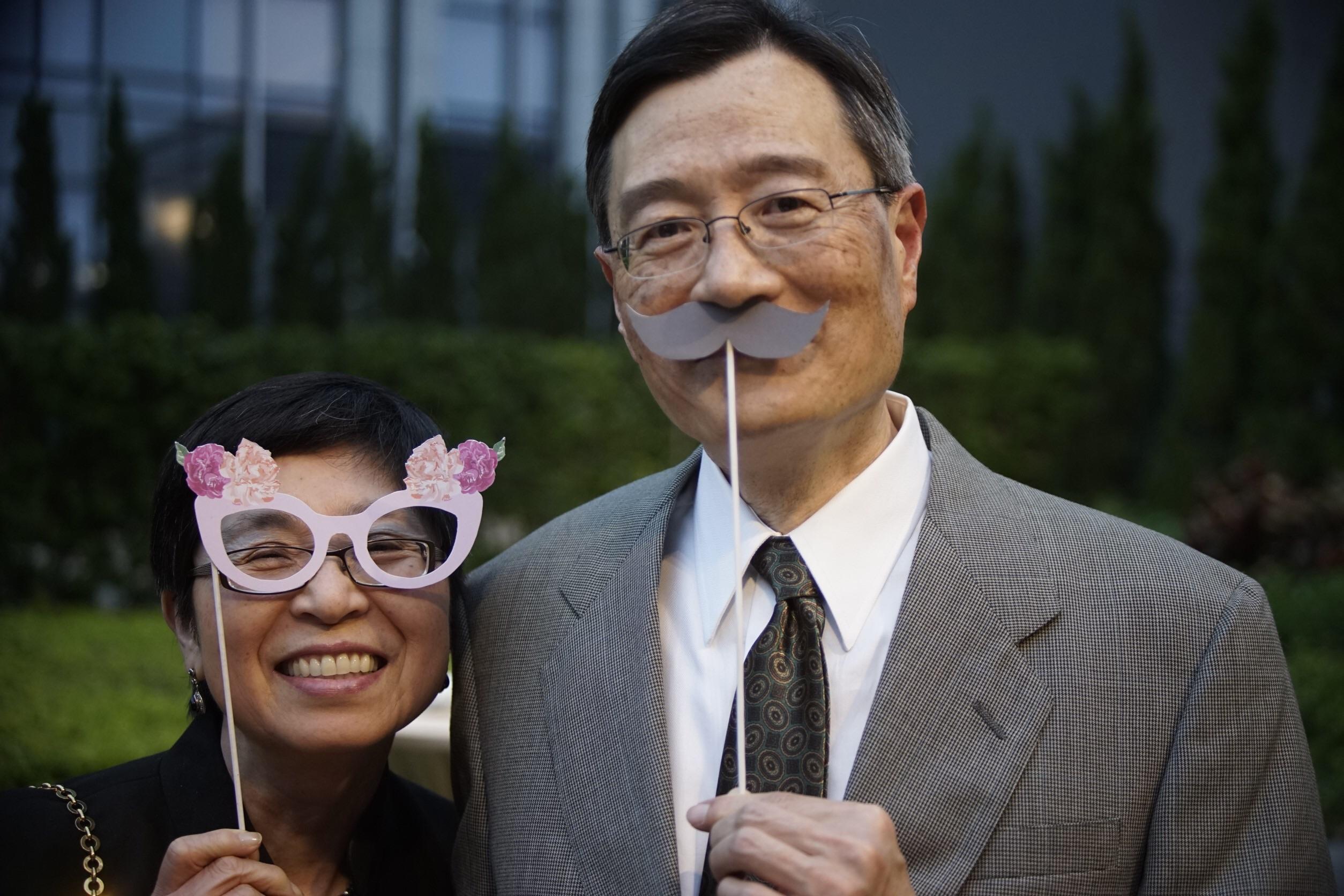 A couple poses together, sharing smiles while holding props at a festive outdoor event.