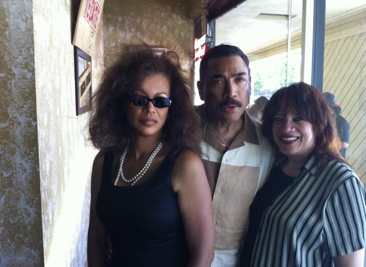 Three friends stand close to each other, enjoying a casual moment at a local gathering.