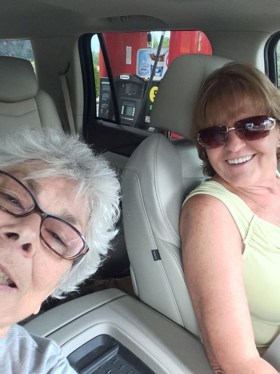 Two friends enjoy each other's company while taking a selfie in a car at a gas station.