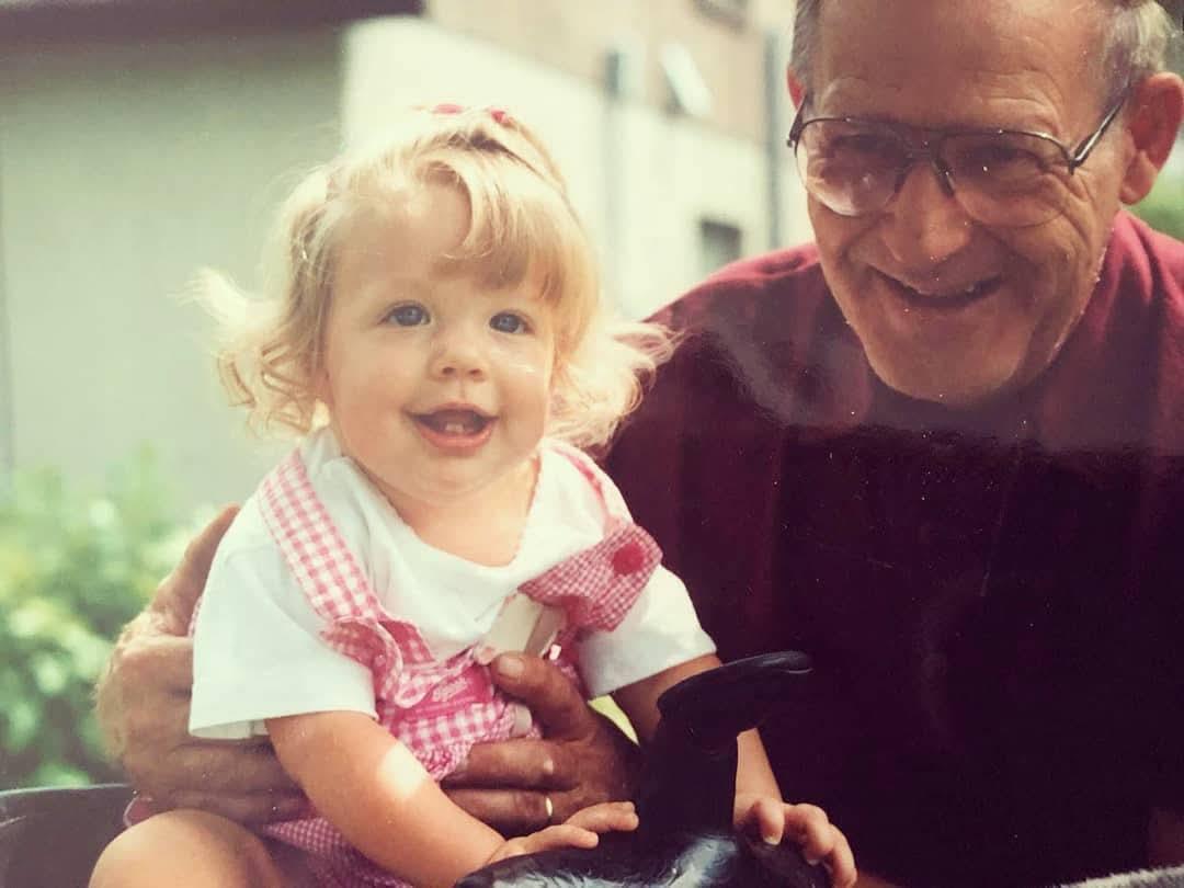 A joyful grandfather holds his smiling granddaughter outside on a warm day, making memories.