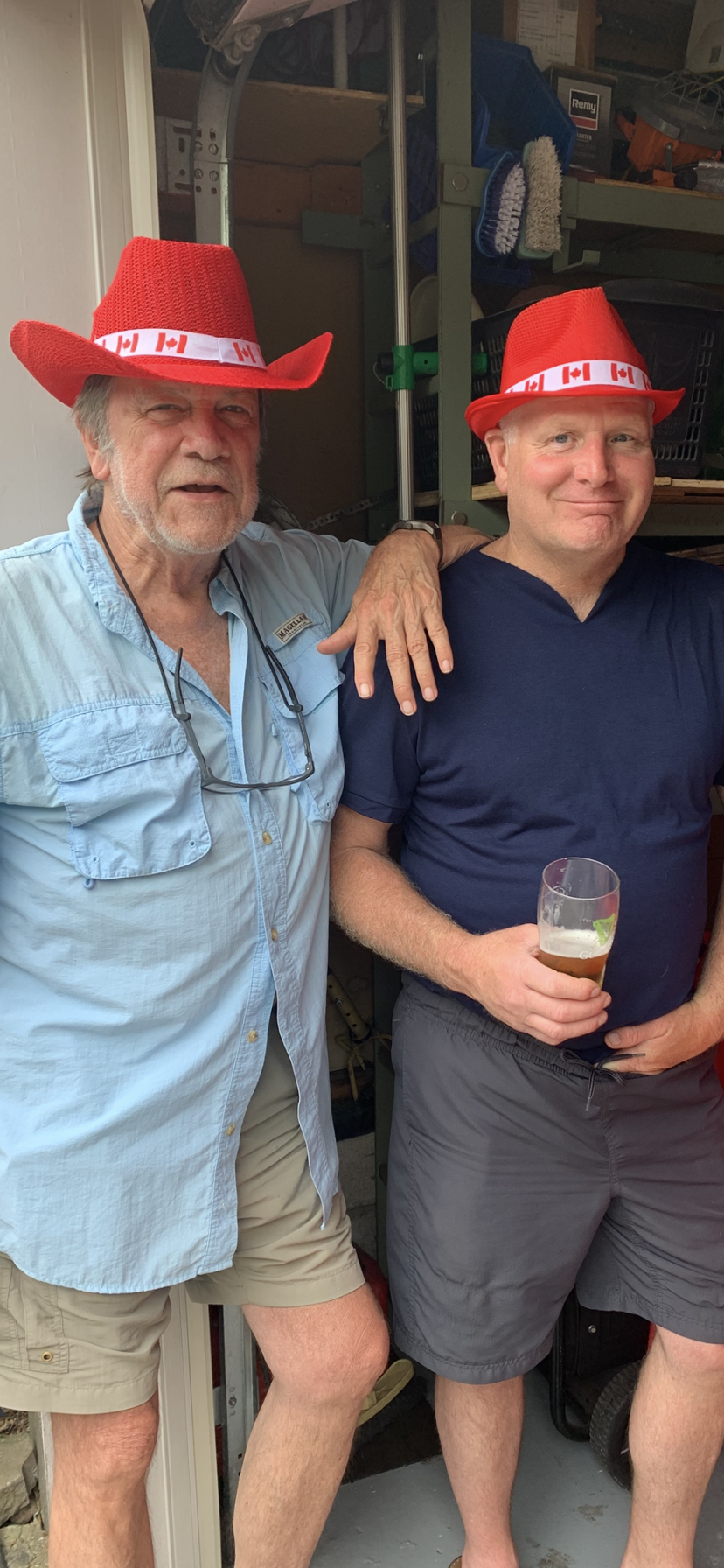 Two friends enjoy a lighthearted moment together inside a garage while wearing festive hats.