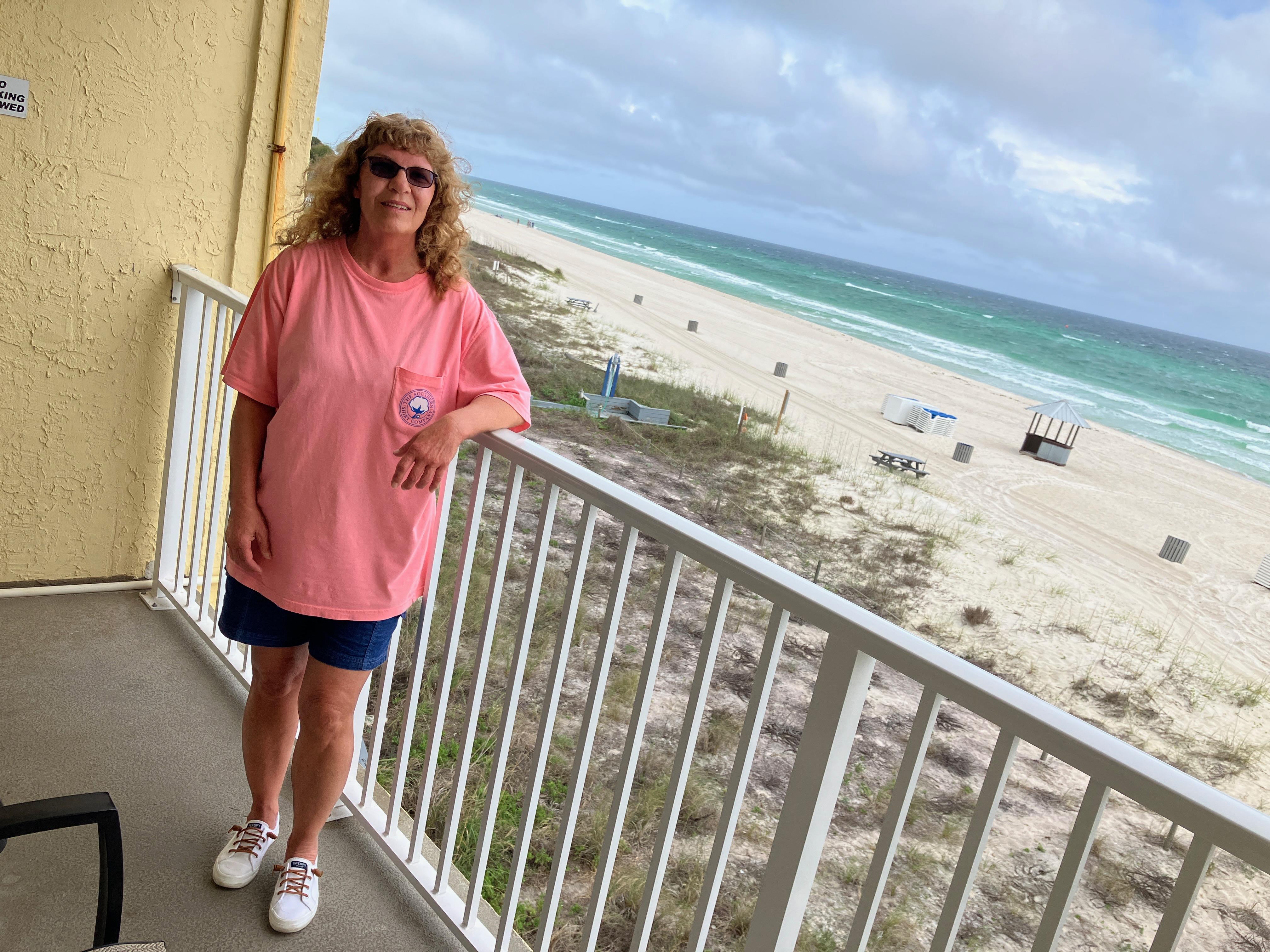 Woman enjoying a coastal view from a balcony, with waves and sandy beach visible below.