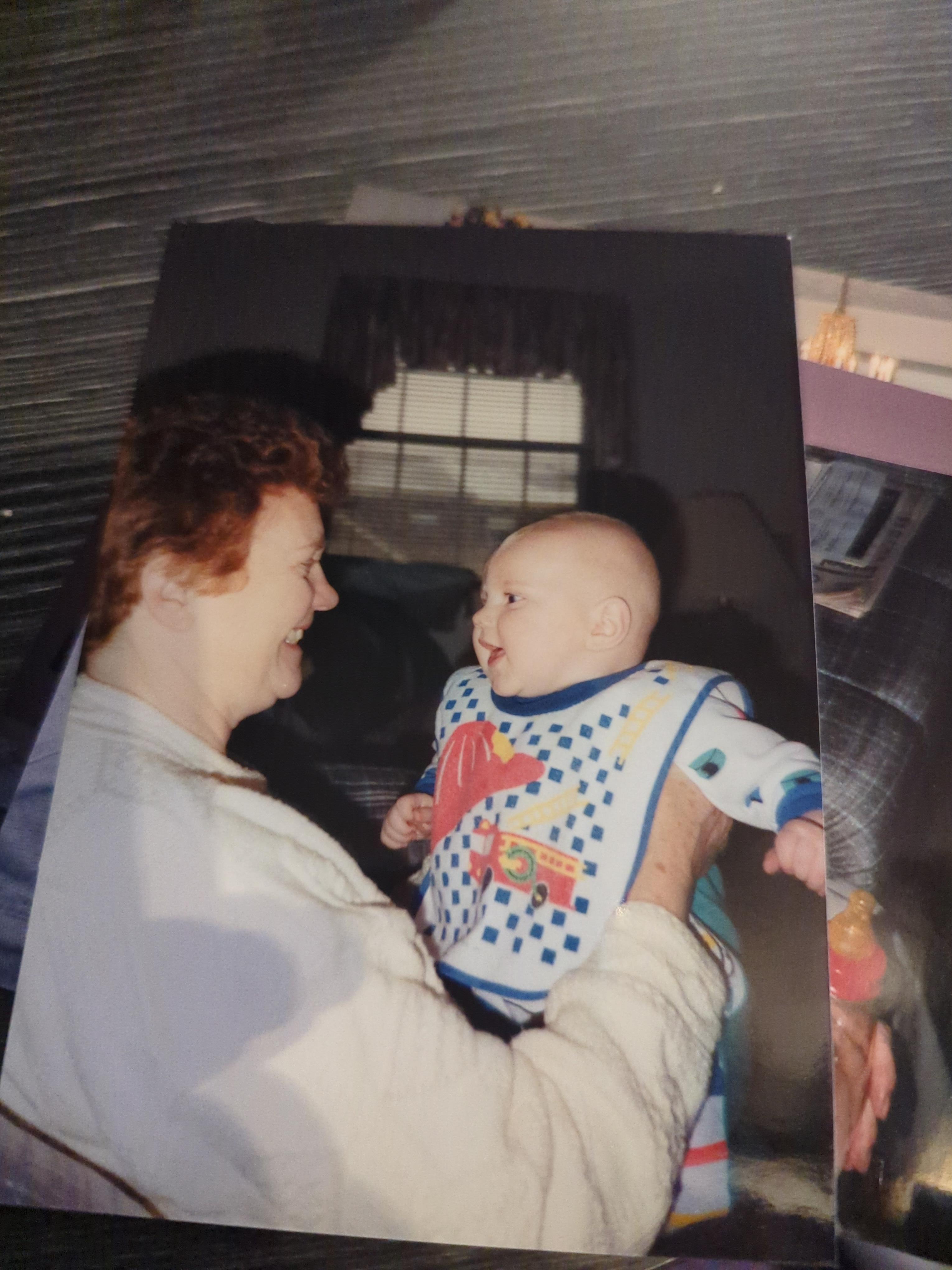 A grandmother shares a warm moment with her baby grandchild, both smiling happily indoors.