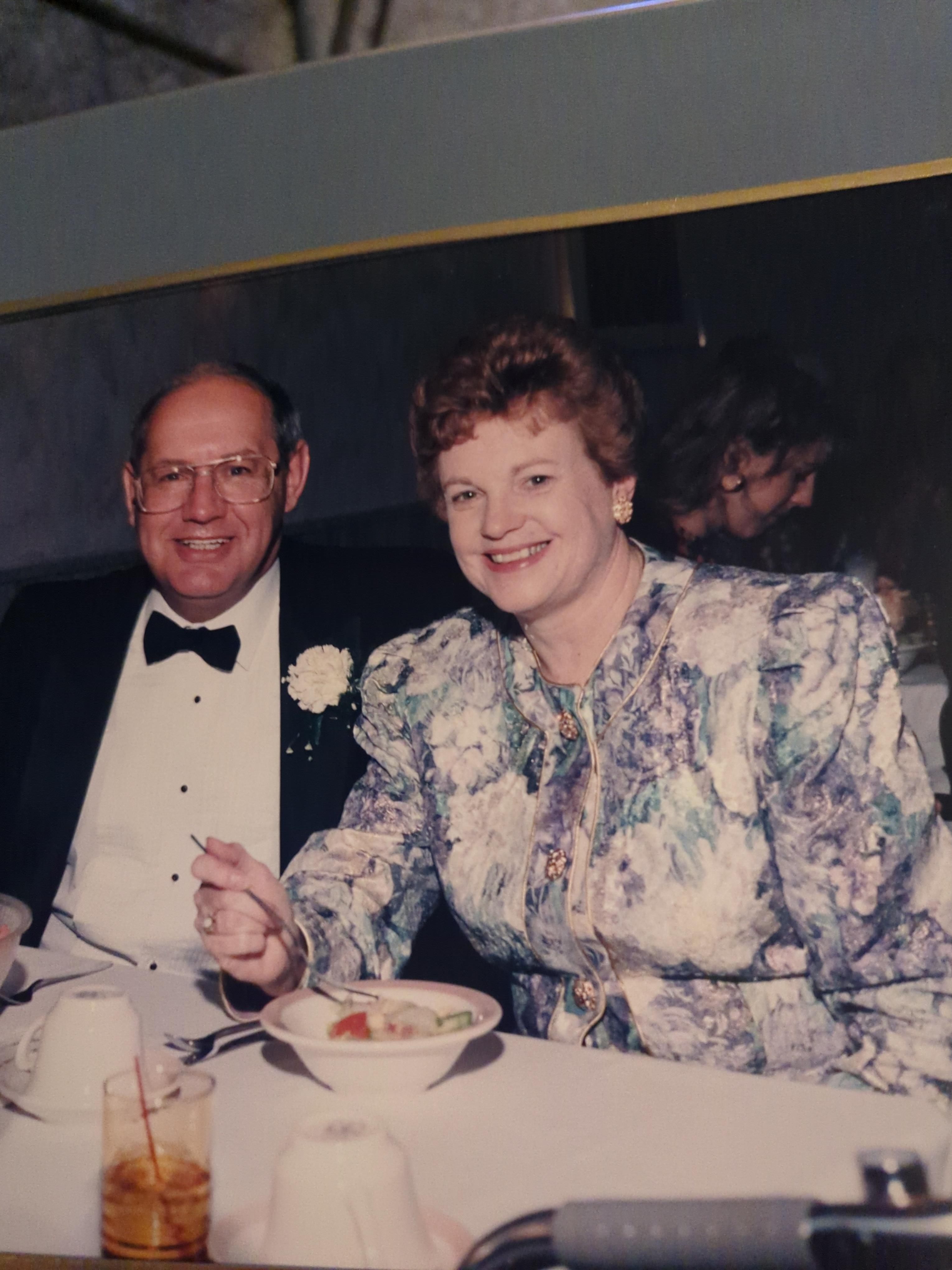 Couple shares a joyful moment at a dinner party, dressed in formal attire in a festive atmosphere.