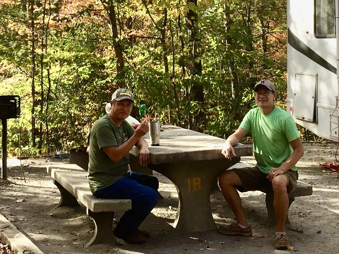 Two men sit together at a stone picnic table, savoring a relaxed moment in nature.