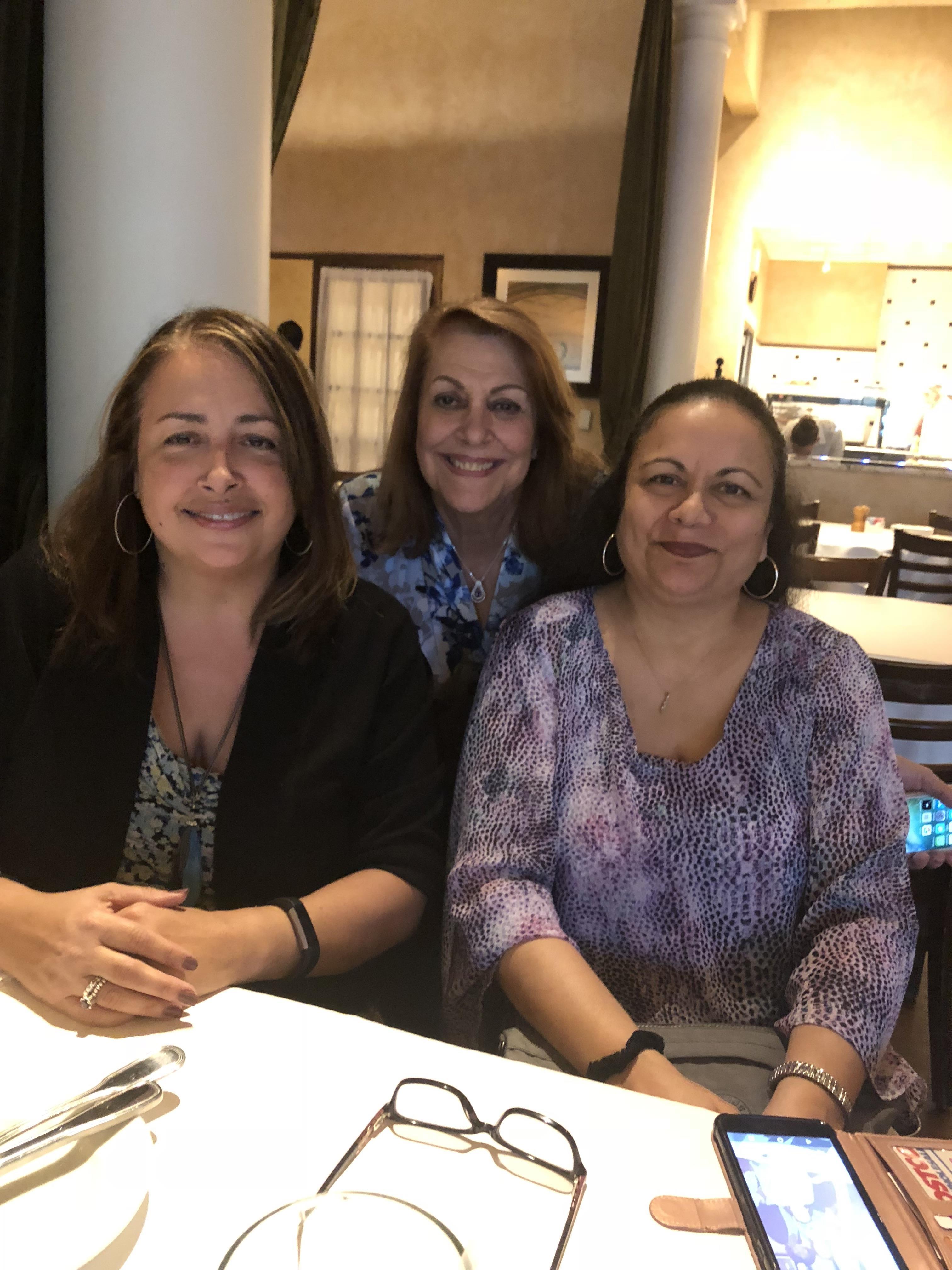 Three women sit together at a restaurant table, smiling and enjoying each other's company.
