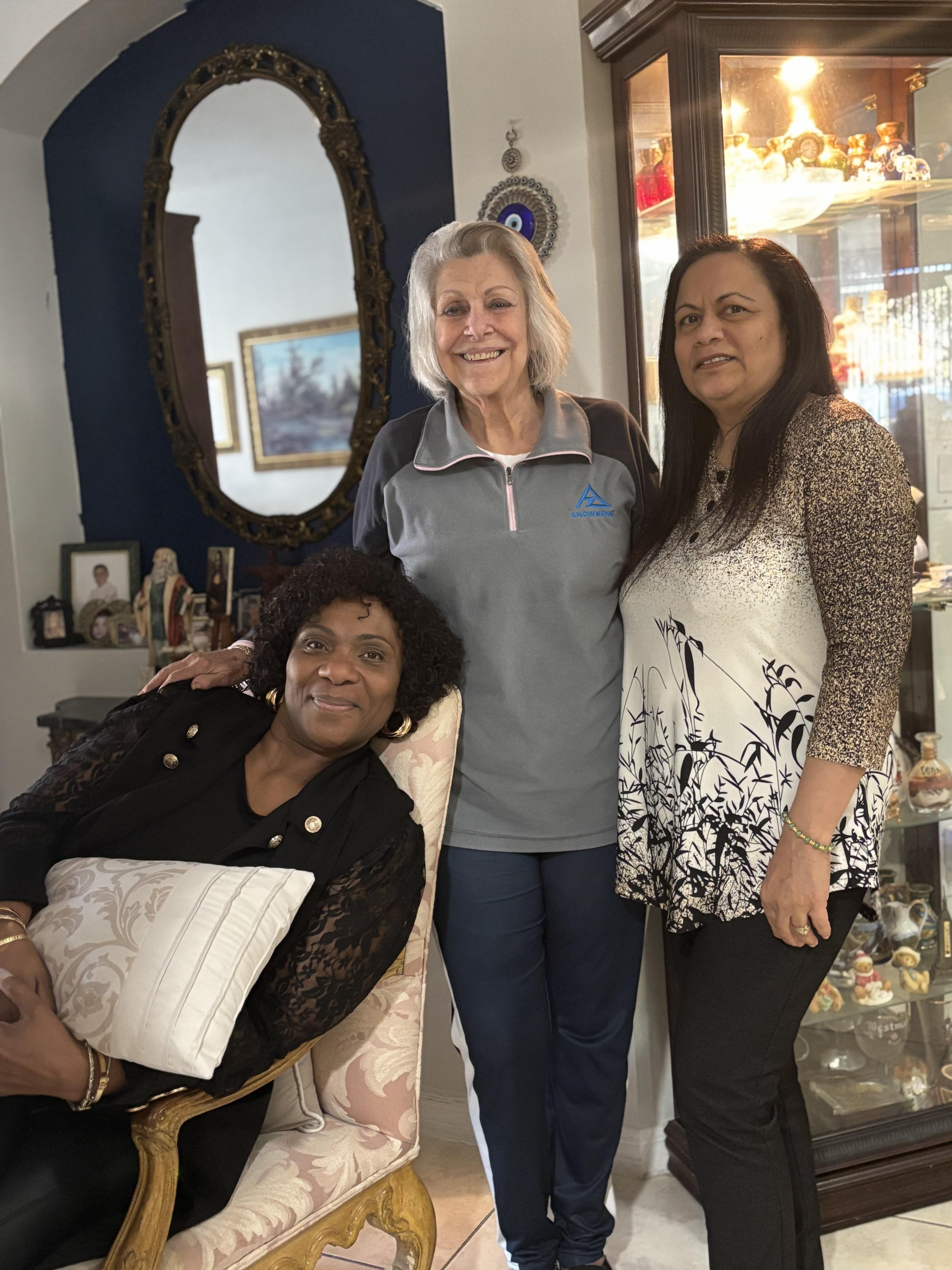 Three women pose together in a welcoming living room, smiling and enjoying each other's company.