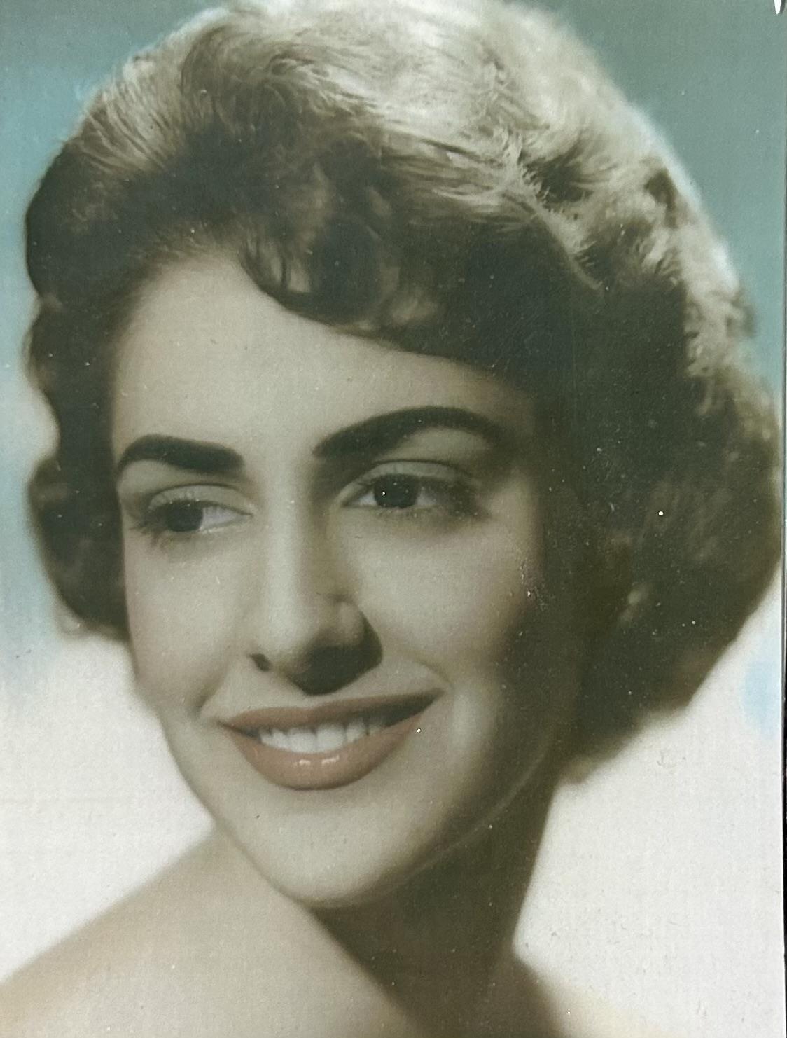 Woman poses gracefully with a warm smile, showcasing a stylish mid-century hairstyle and makeup.