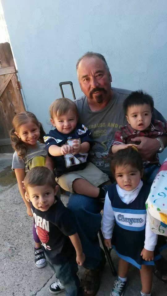 A grandfather sits surrounded by six happy children, showcasing a heartwarming family bond.