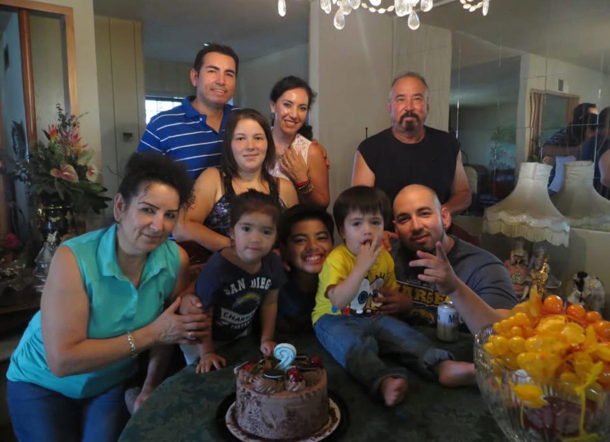 A group of family members gathers around a decorated table enjoying a cake together.