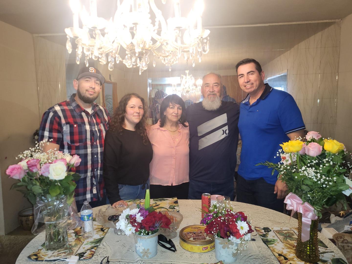 Friends and family enjoy time together around a table filled with flowers and treats in a warm home.