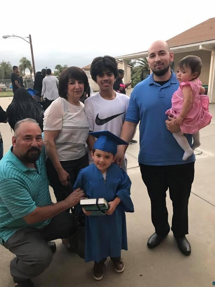 Family celebrates outdoors with a proud young graduate in cap and gown.