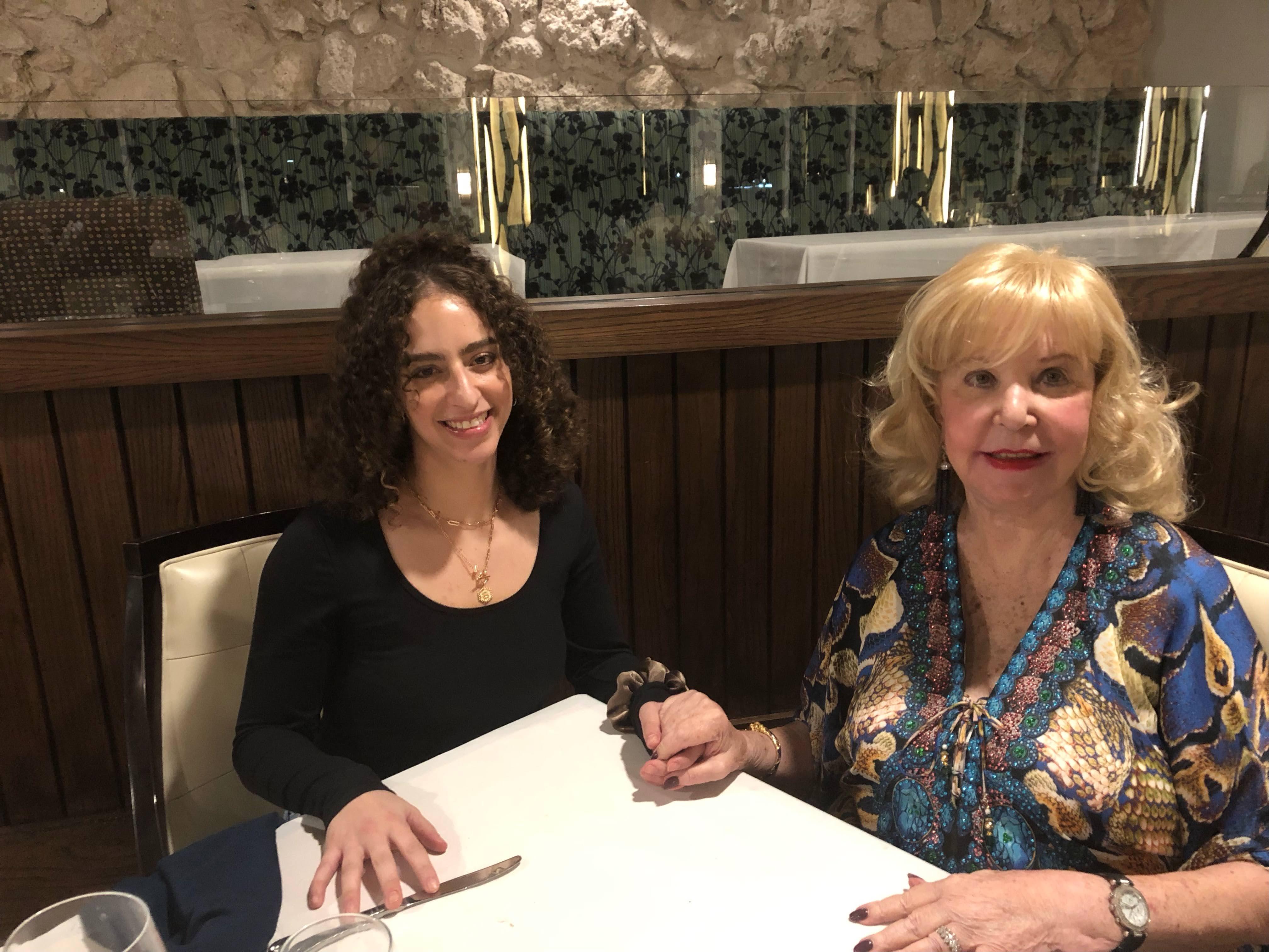 Two women sit at a table holding hands, sharing a meaningful moment during dinner.