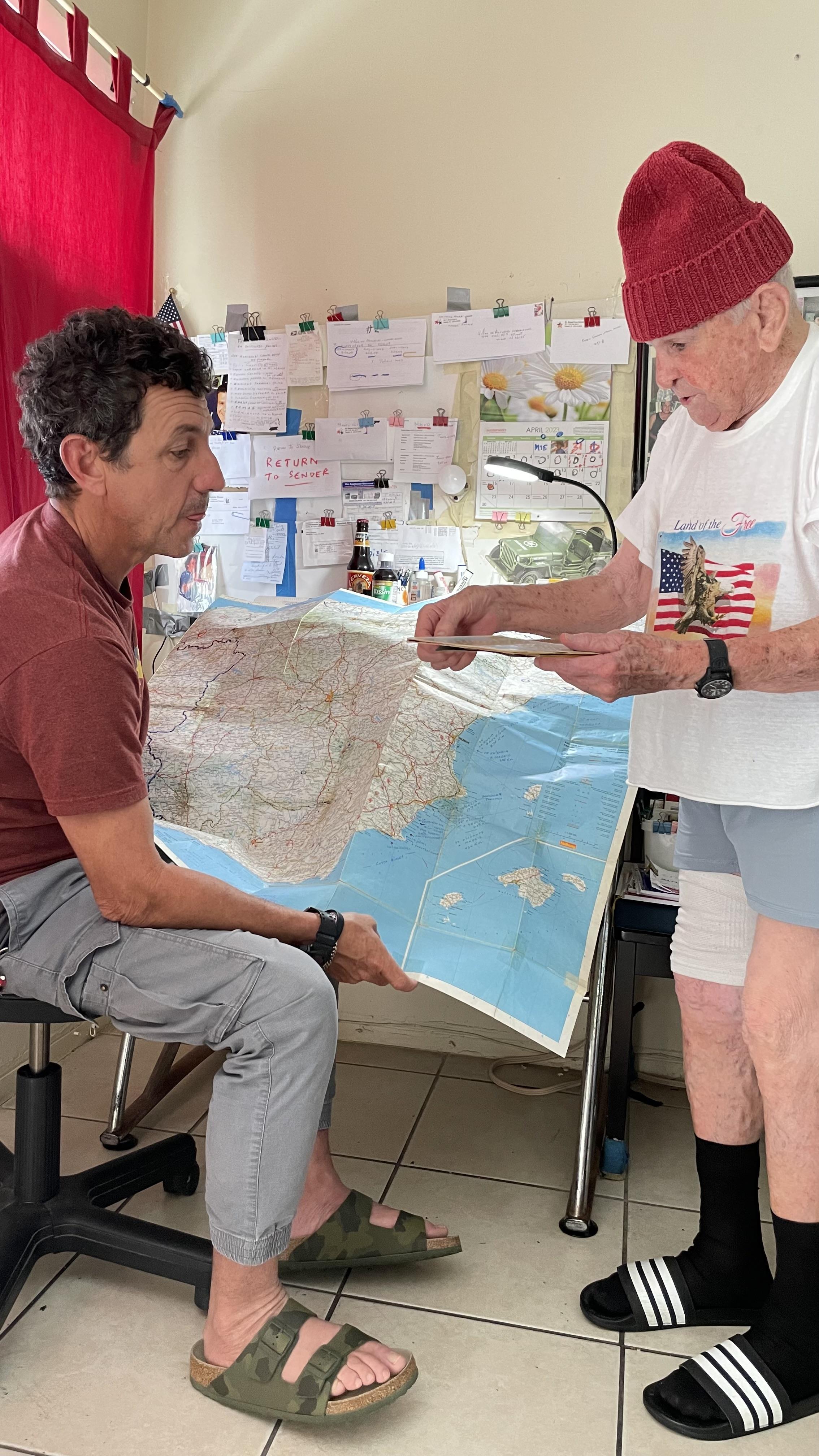 Two individuals examine a large map, discussing details in a light-filled room filled with notes.